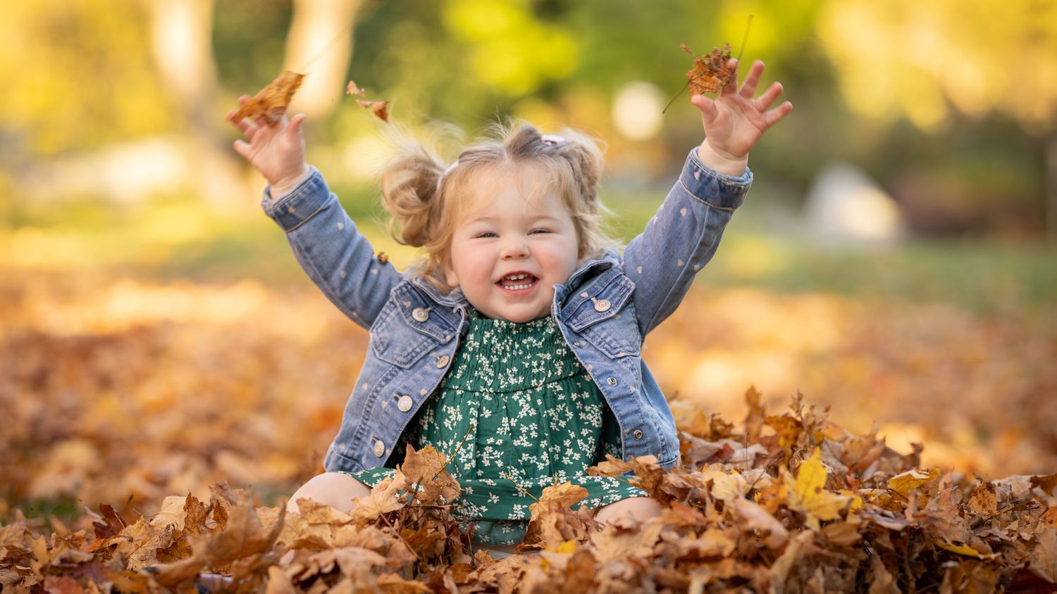 A young child plays joyfully in a pile of colorful autumn leaves on a sunny fall day.