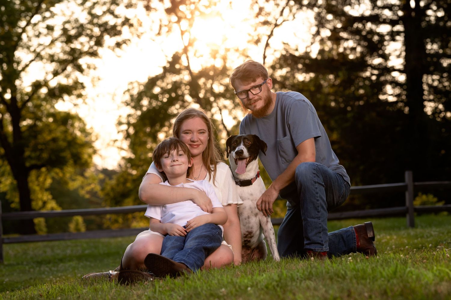 A family and their dog relaxing together on a grassy hill during golden hour sunset.