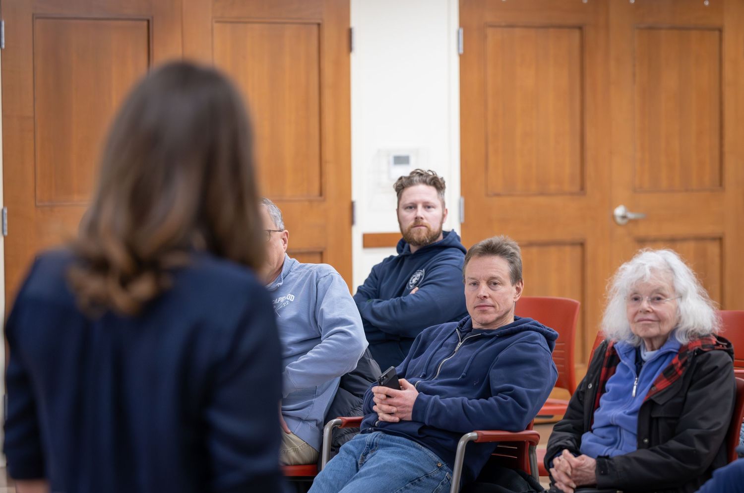 A group of people sit in rows of chairs during an indoor meeting or presentation.