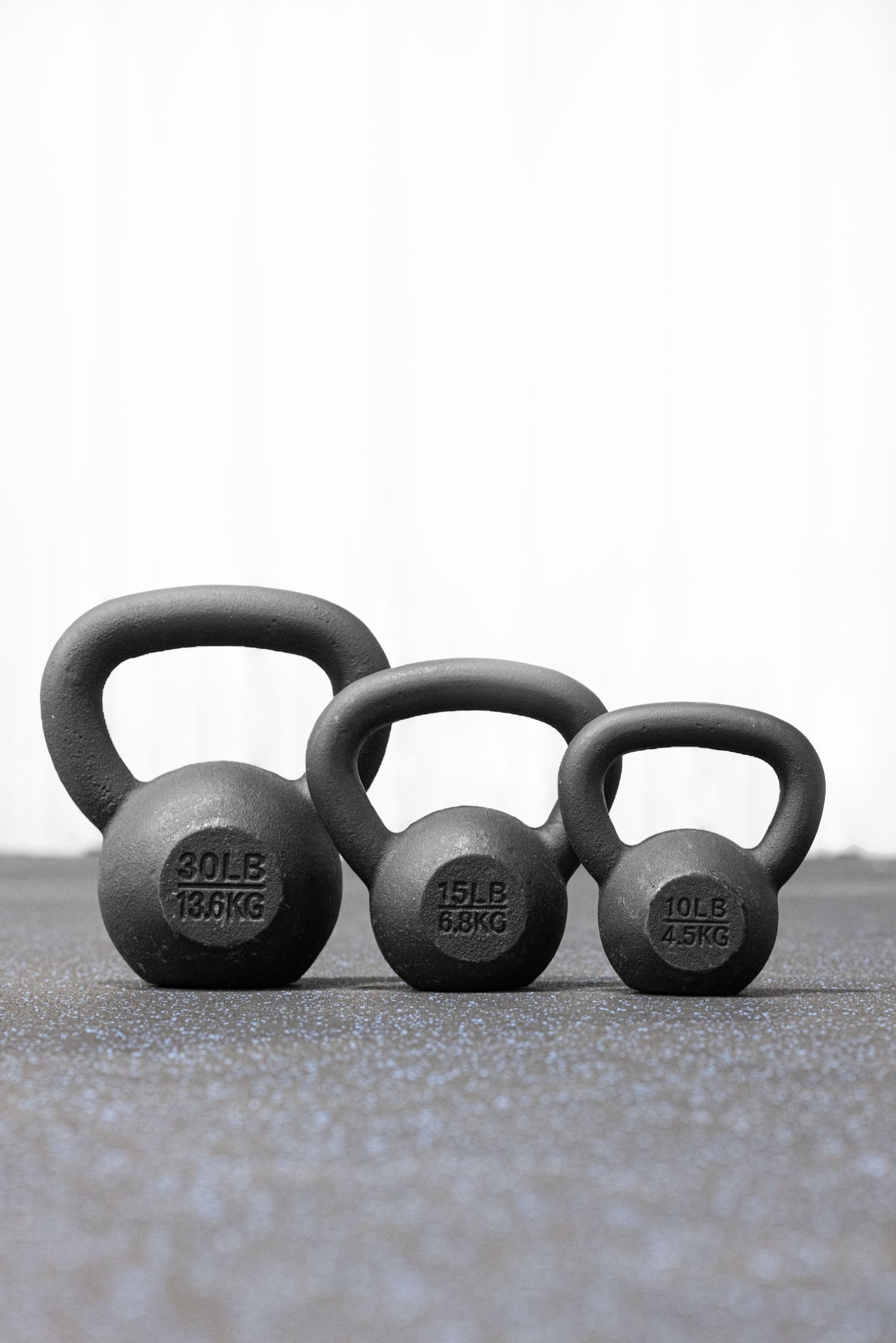 A row of black kettlebells of varying sizes lined up on a gray surface showing ascending weight progression.