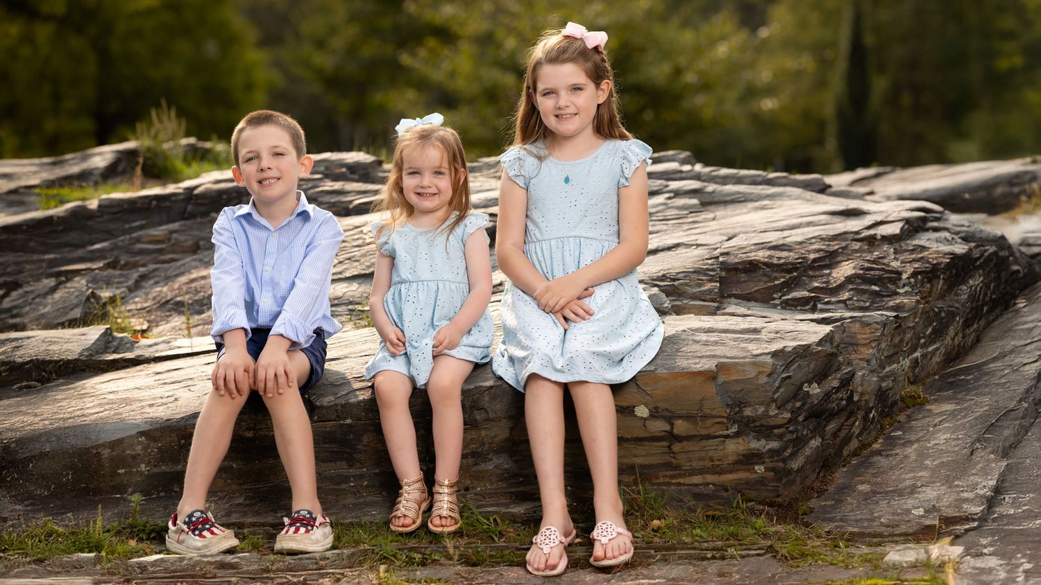 Children in coordinated blue and white outfits sit together on a large rock formation outdoors.
