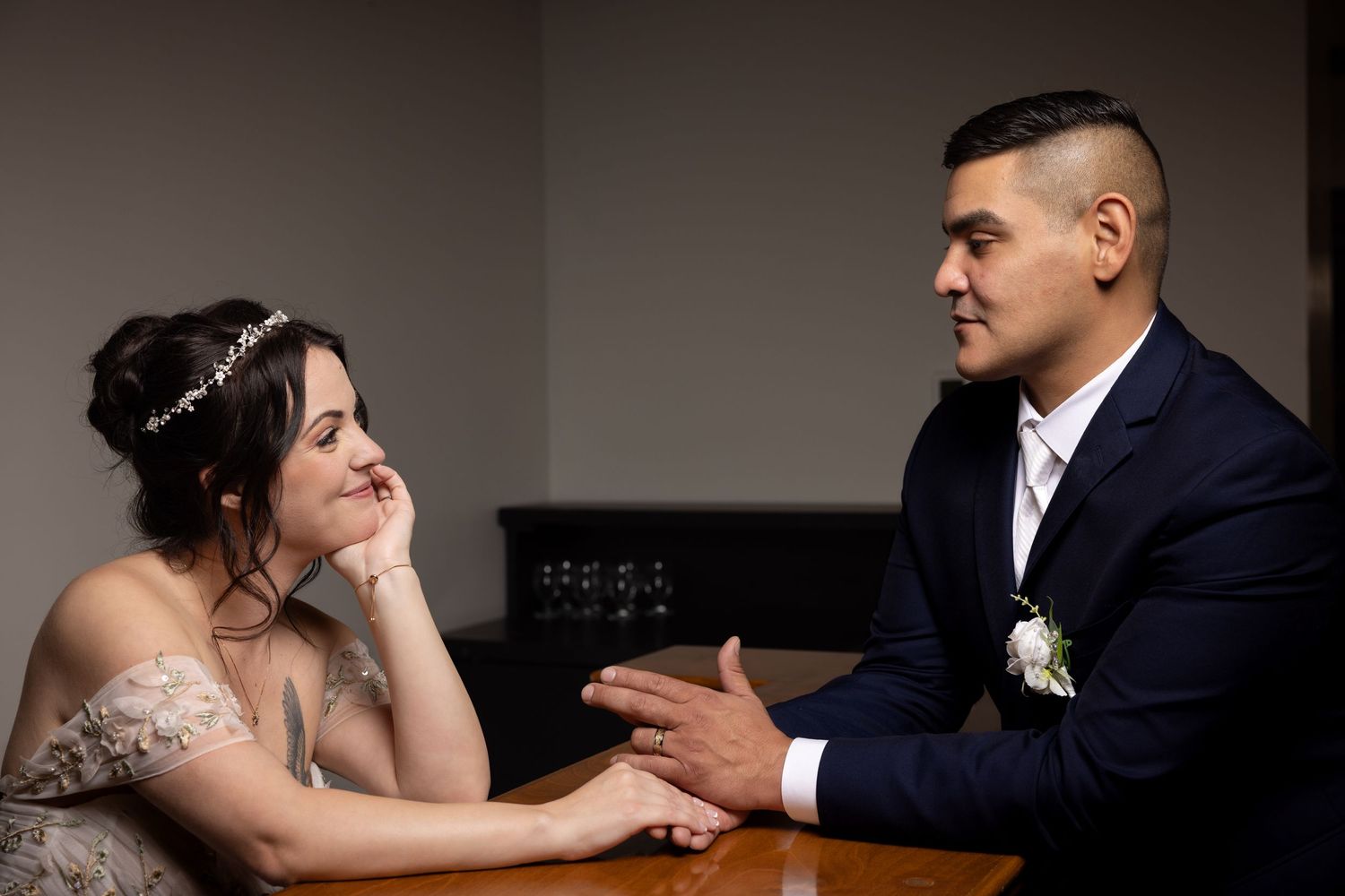 Bride and groom share intimate moment at table during wedding reception in dimly lit room.