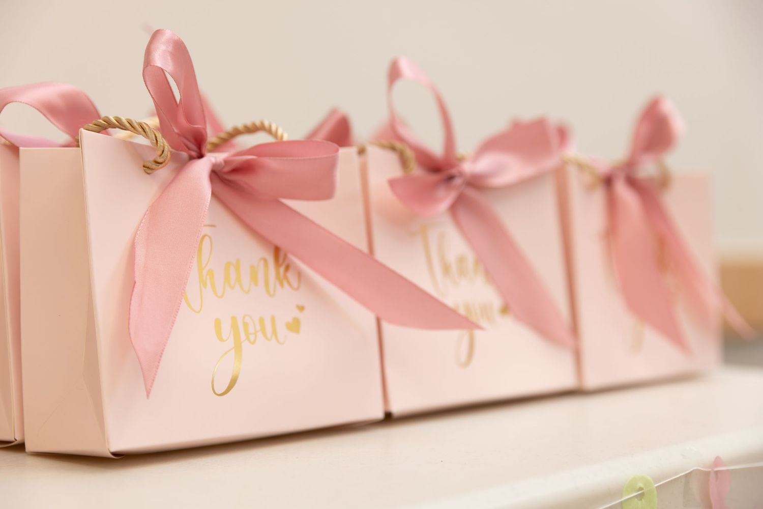 Pink gift boxes with satin bows arranged in a row on white surface create an elegant display.