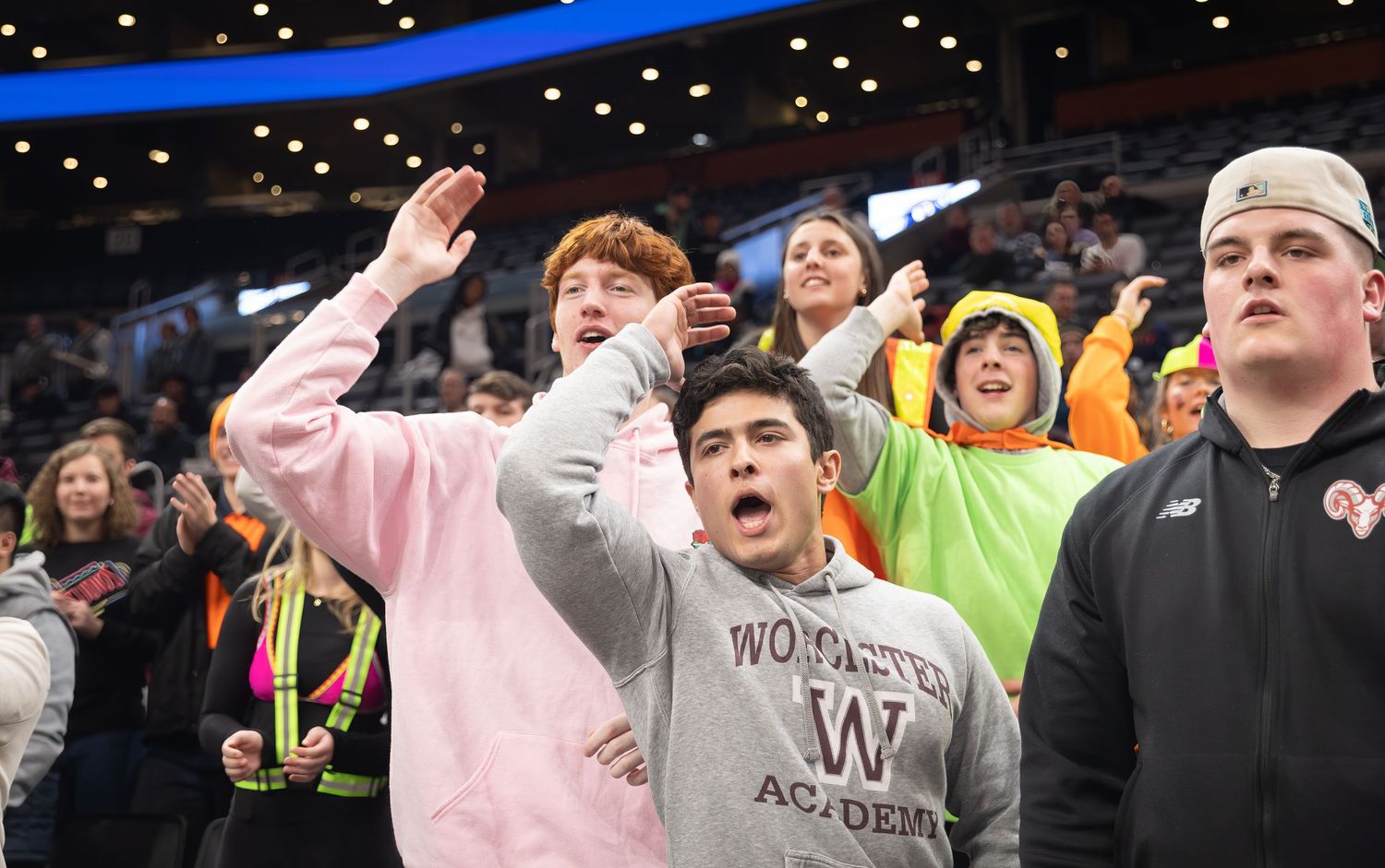 Excited sports fans in the crowd react emotionally during an intense game moment at an indoor arena.