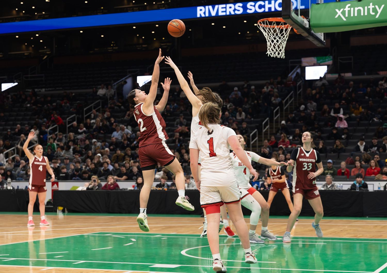 Basketball players compete for a rebound during an intense game at Rivers School with Xfinity signage visible in background.