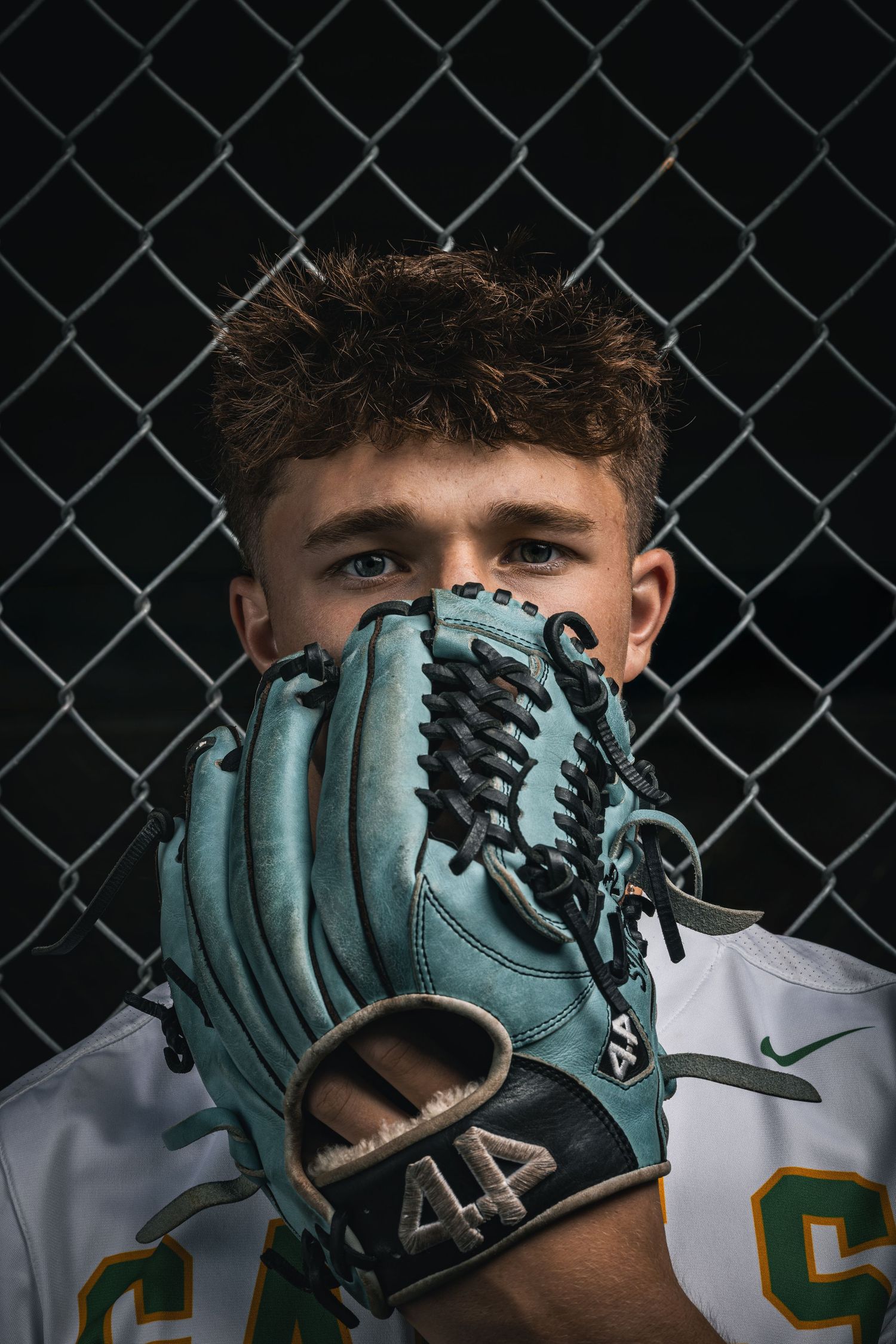 Baseball player holds up turquoise glove in front of face while wearing white uniform with jersey number visible.