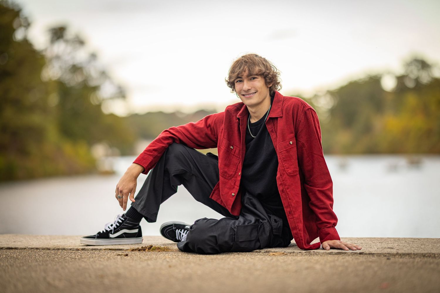A person in a red jacket reclines on a paved surface during golden hour.