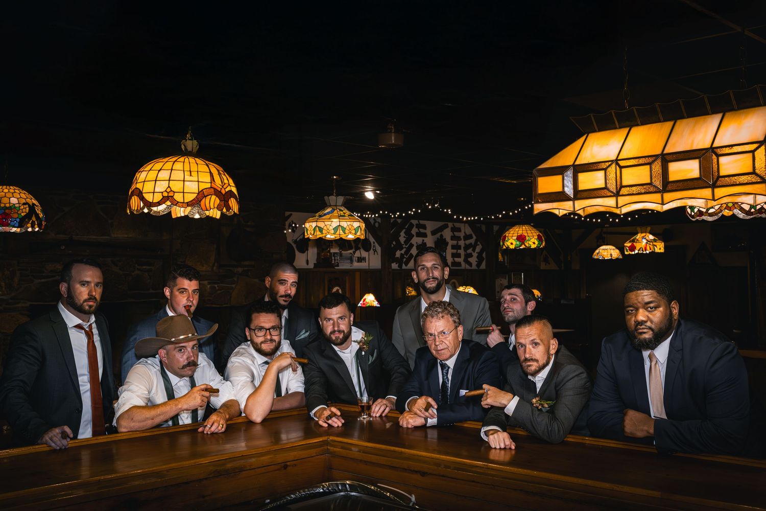 People gather at a dimly lit bar with stained glass lamps overhead, creating a warm and intimate atmosphere.