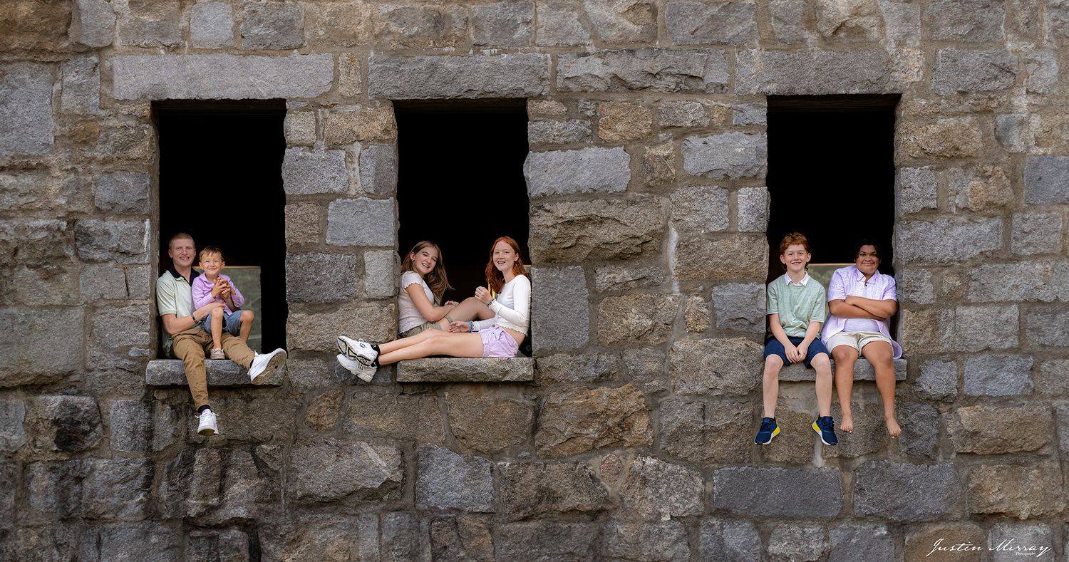 People sit in stone window openings of an ancient castle wall, creating a unique architectural composition.
