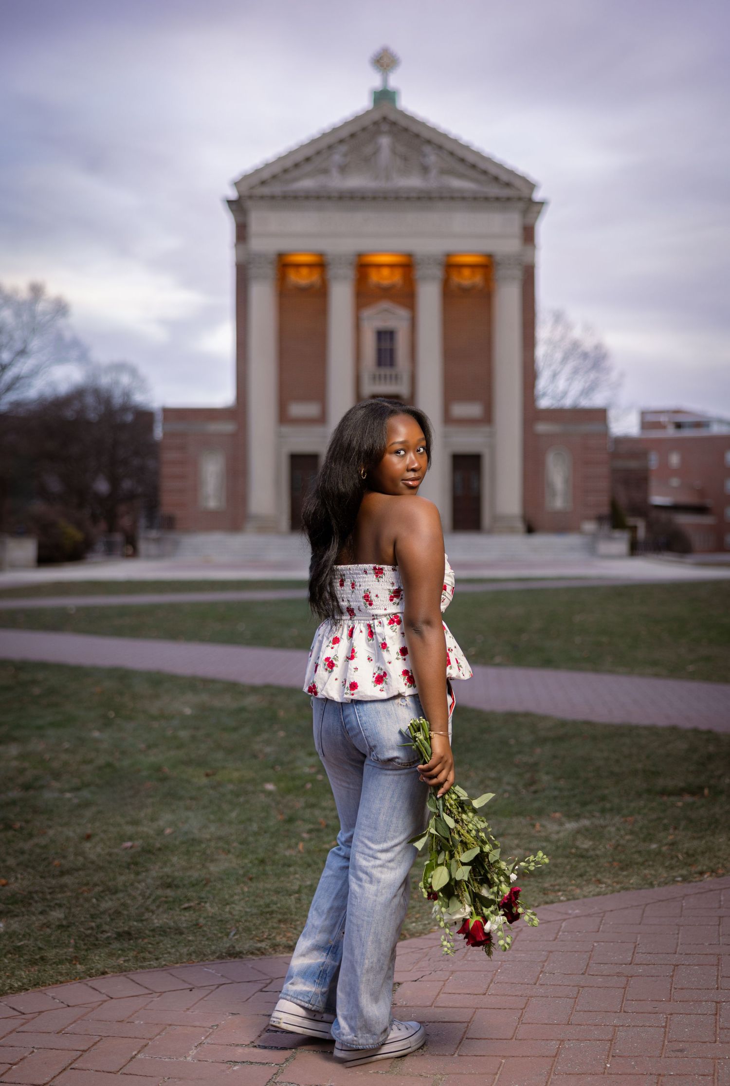A couple embraces in front of a historic brick church building with columns on an overcast day.