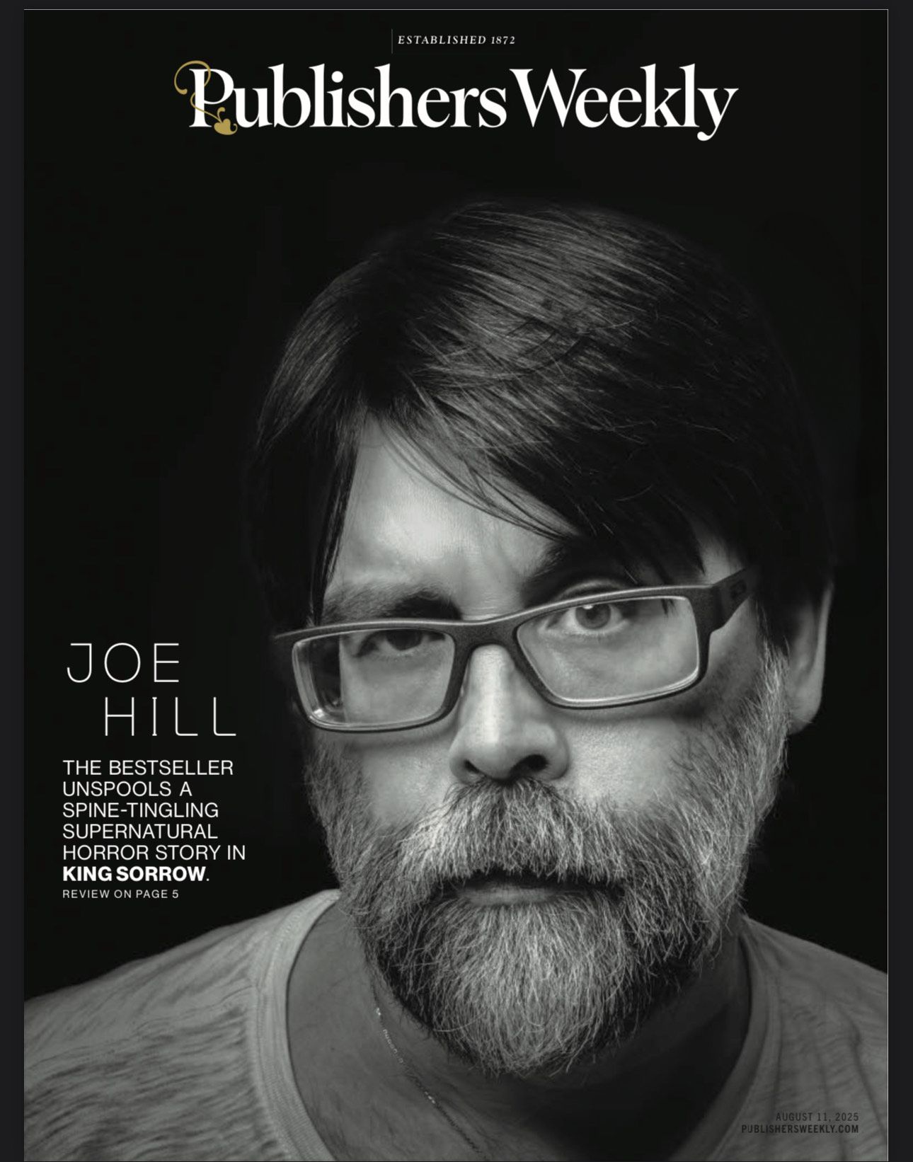Black and white portrait photograph of a bearded person wearing glasses against a dark background.