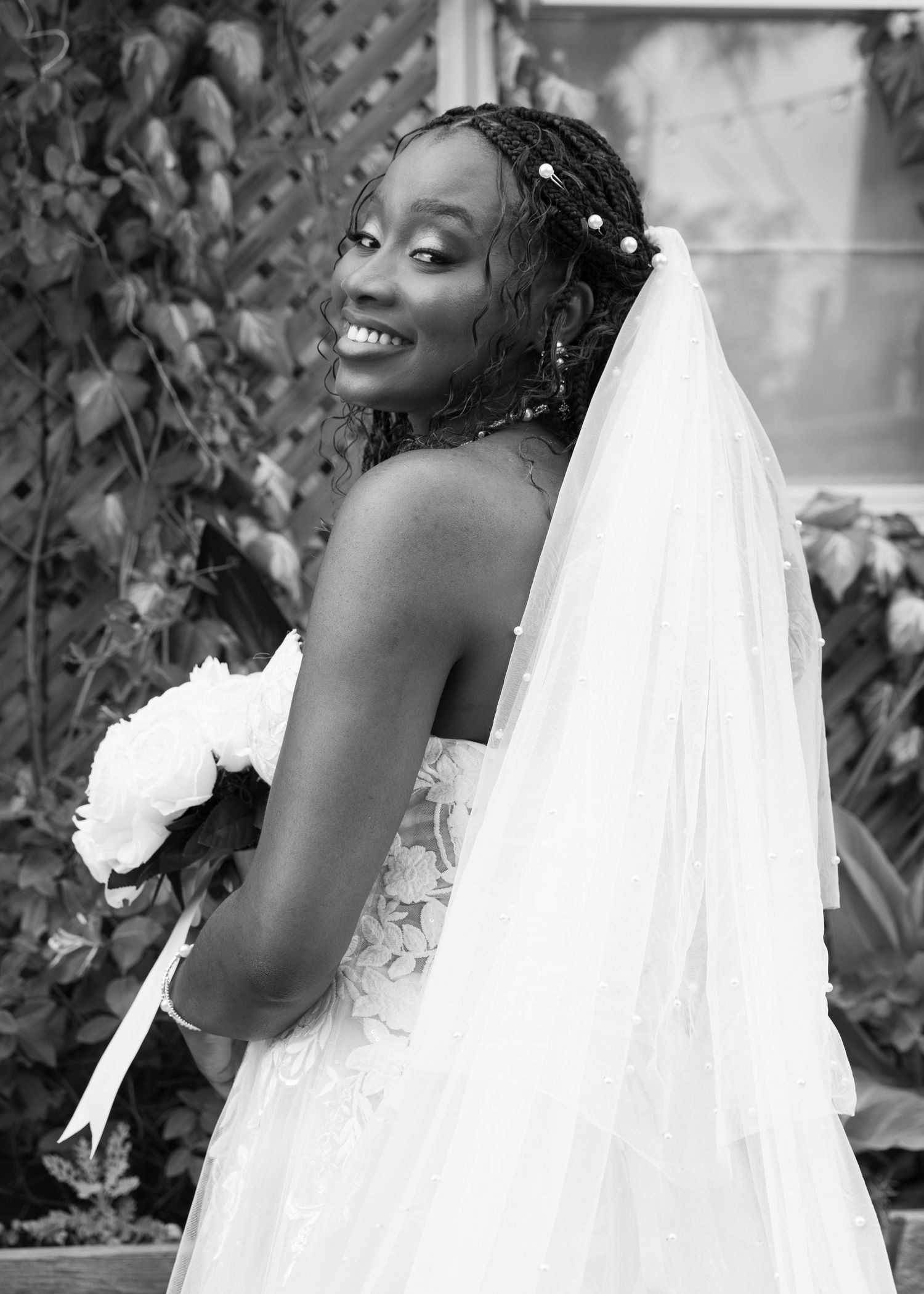 A joyful bride in a white strapless wedding gown poses with a bouquet and veil in a black and white portrait.