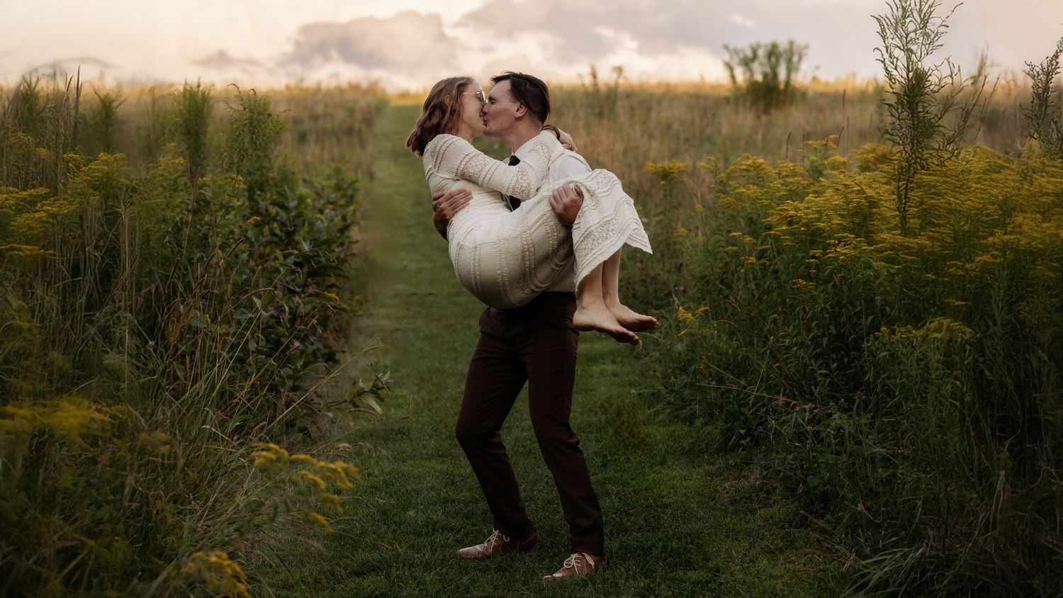 A couple embraces in a golden field during sunset while dancing together in romantic outdoor photos.