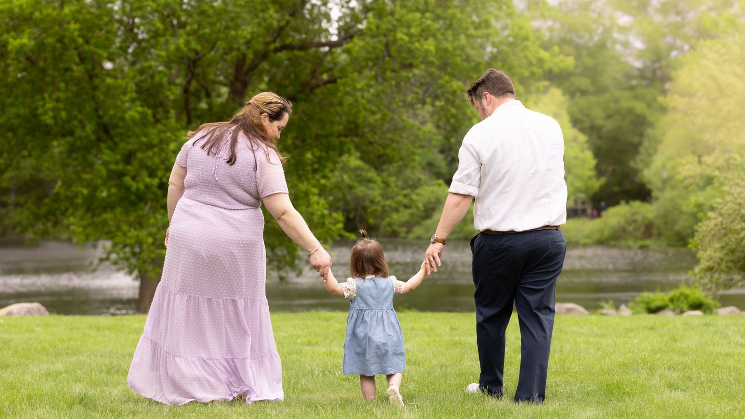 A family holding hands walks together through a lush green park on a sunny spring day.