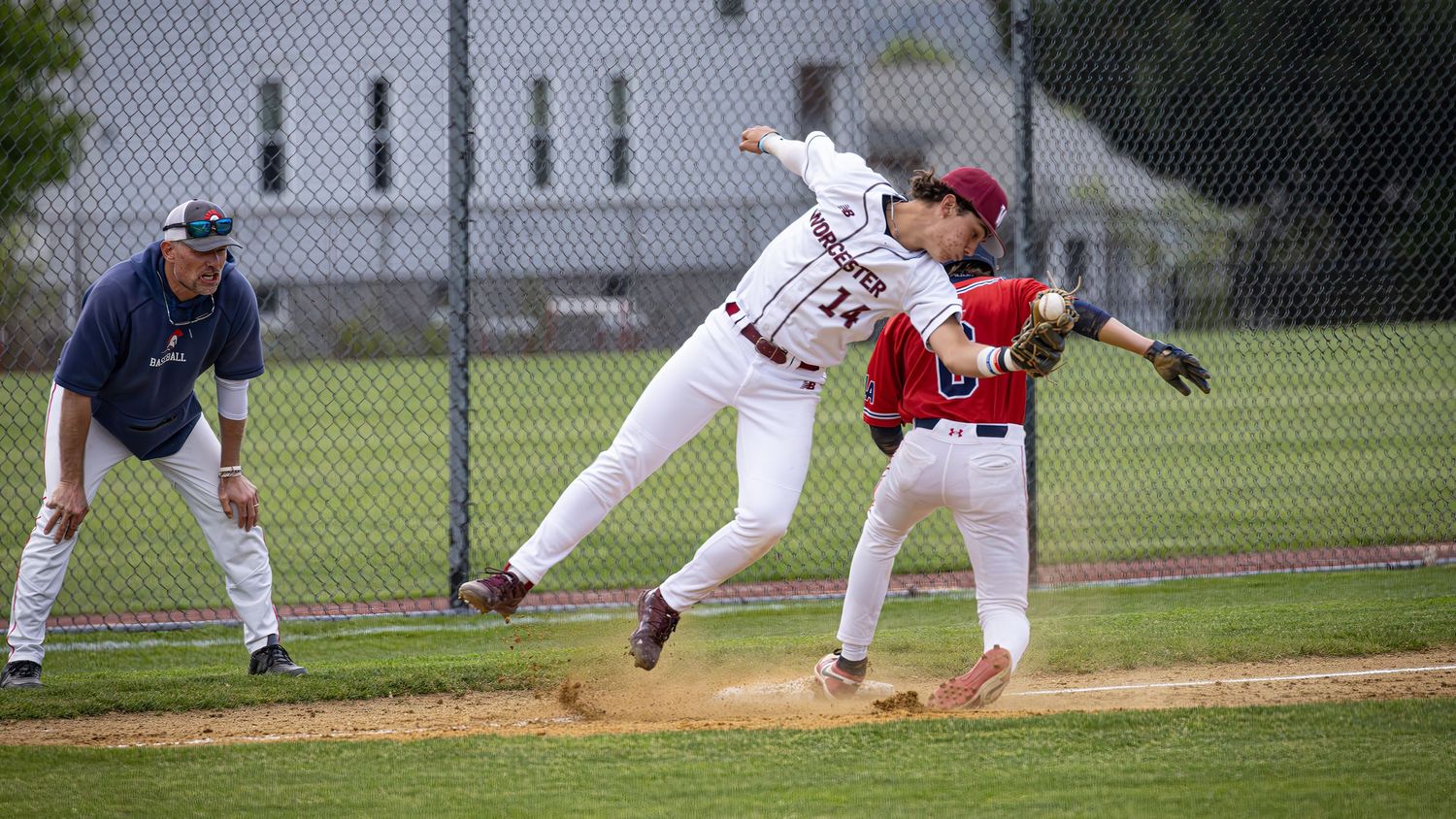 Baseball player sliding into base during competitive game while fielder attempts to make the tag.