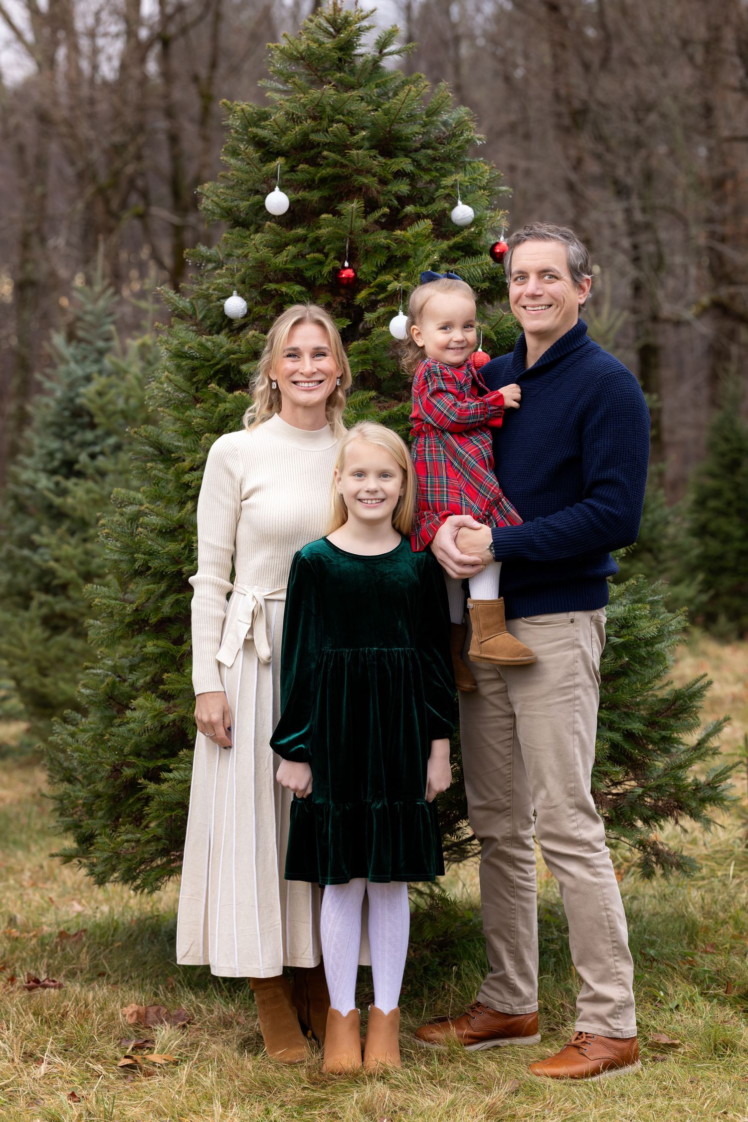 A family poses together among evergreen trees at a Christmas tree farm on a winter day.