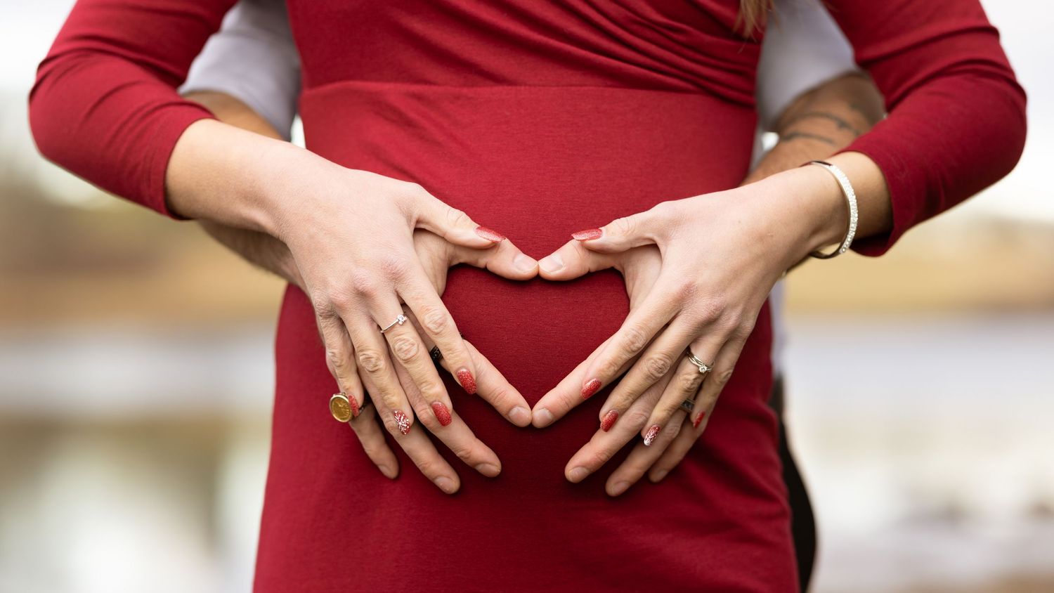 A series of close-up shots showing hands making heart shapes against a red dress background.