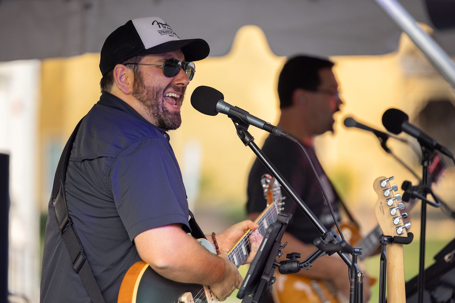 Musicians perform on stage with microphones and instruments during an outdoor concert event.