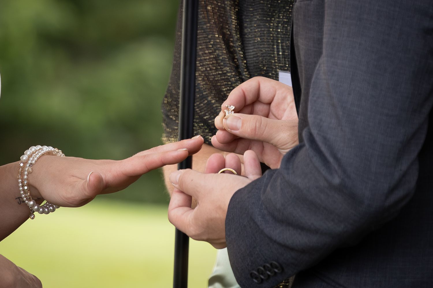 Close-up sequence of hands exchanging rings during an outdoor wedding ceremony.