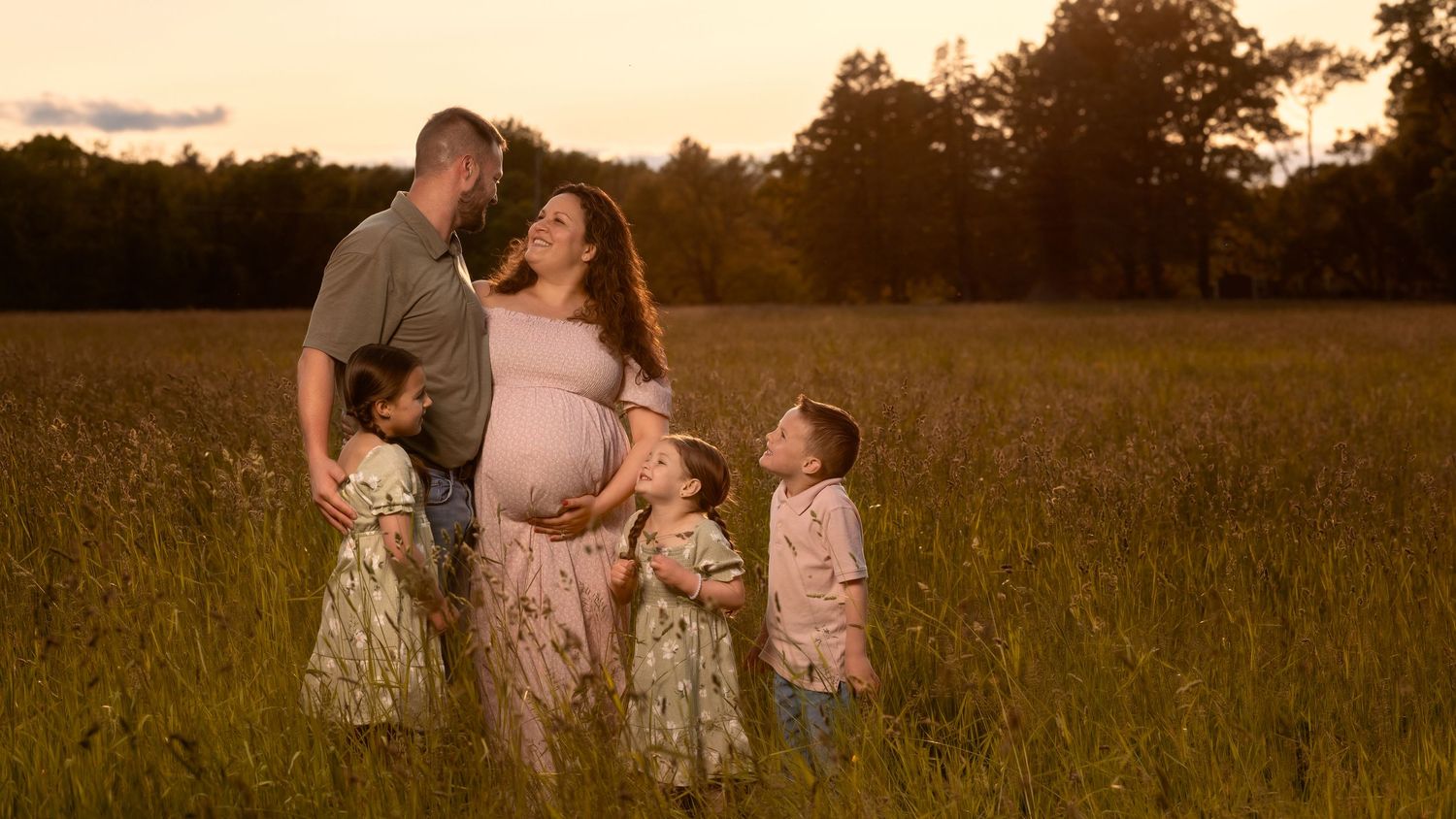 A family wearing coordinated floral outfits walks together in a golden field at sunset.