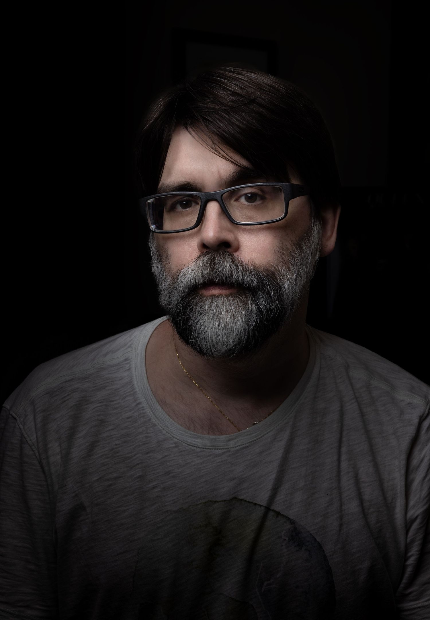 Dramatic black and white portrait series showing a bearded person wearing glasses and a gray t-shirt from different angles.