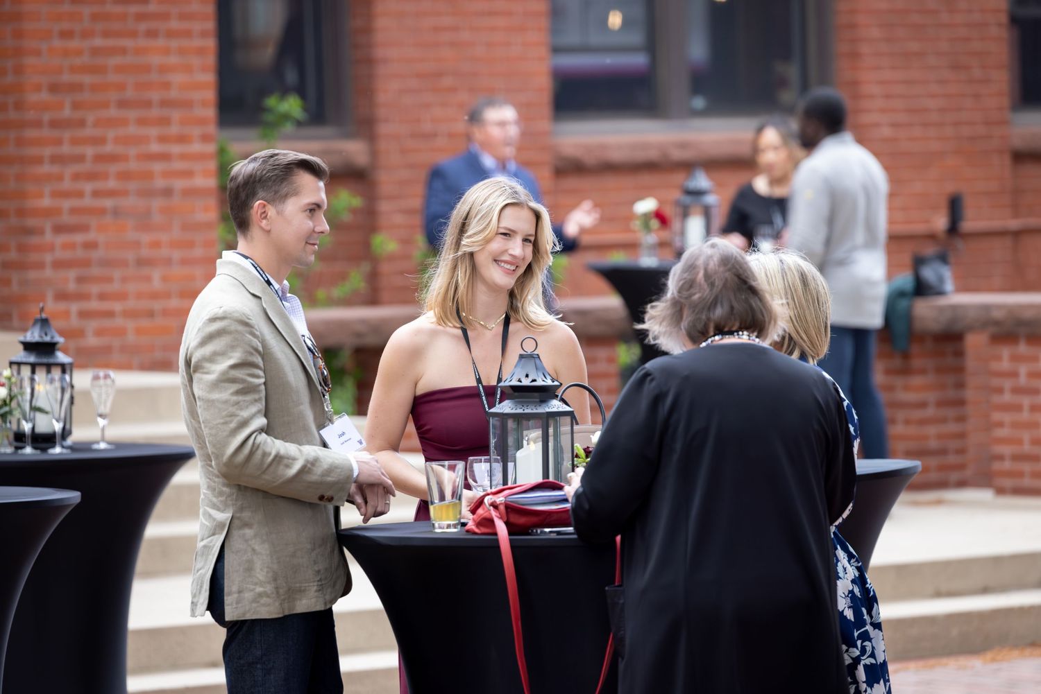 People gather and socialize at an outdoor dining area with brick buildings in the background.