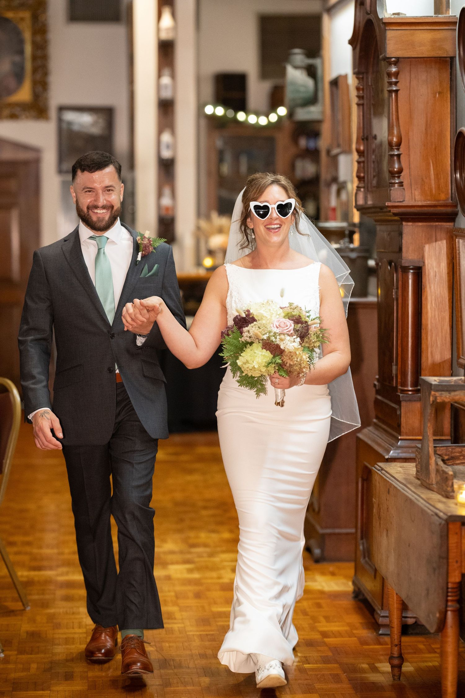 Wedding party walks down wooden aisle in church with elegant decor and warm lighting.