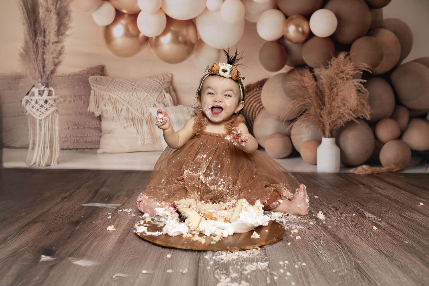 A cake smash photo session setup with neutral balloons and decorations on a wooden floor.