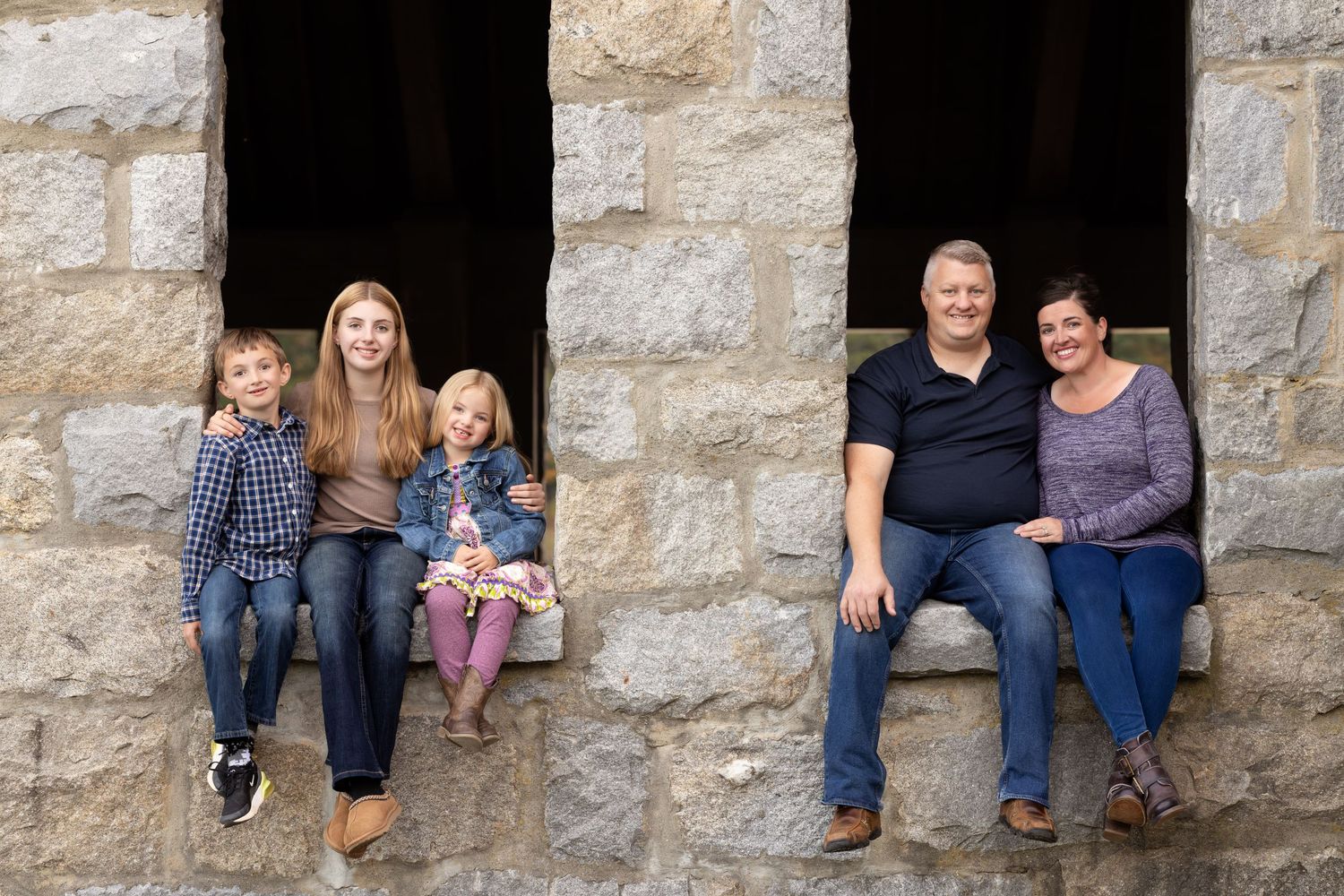 Family members sit in stone window alcoves of an old building for a creative outdoor portrait session.