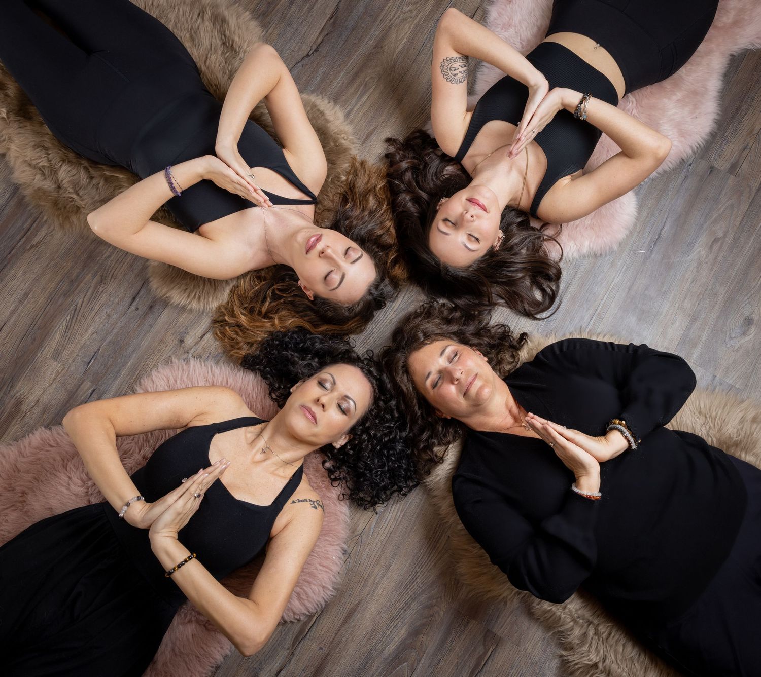 Dancers in black outfits lying on wooden floor in artistic formation with hair spread out during contemporary performance.