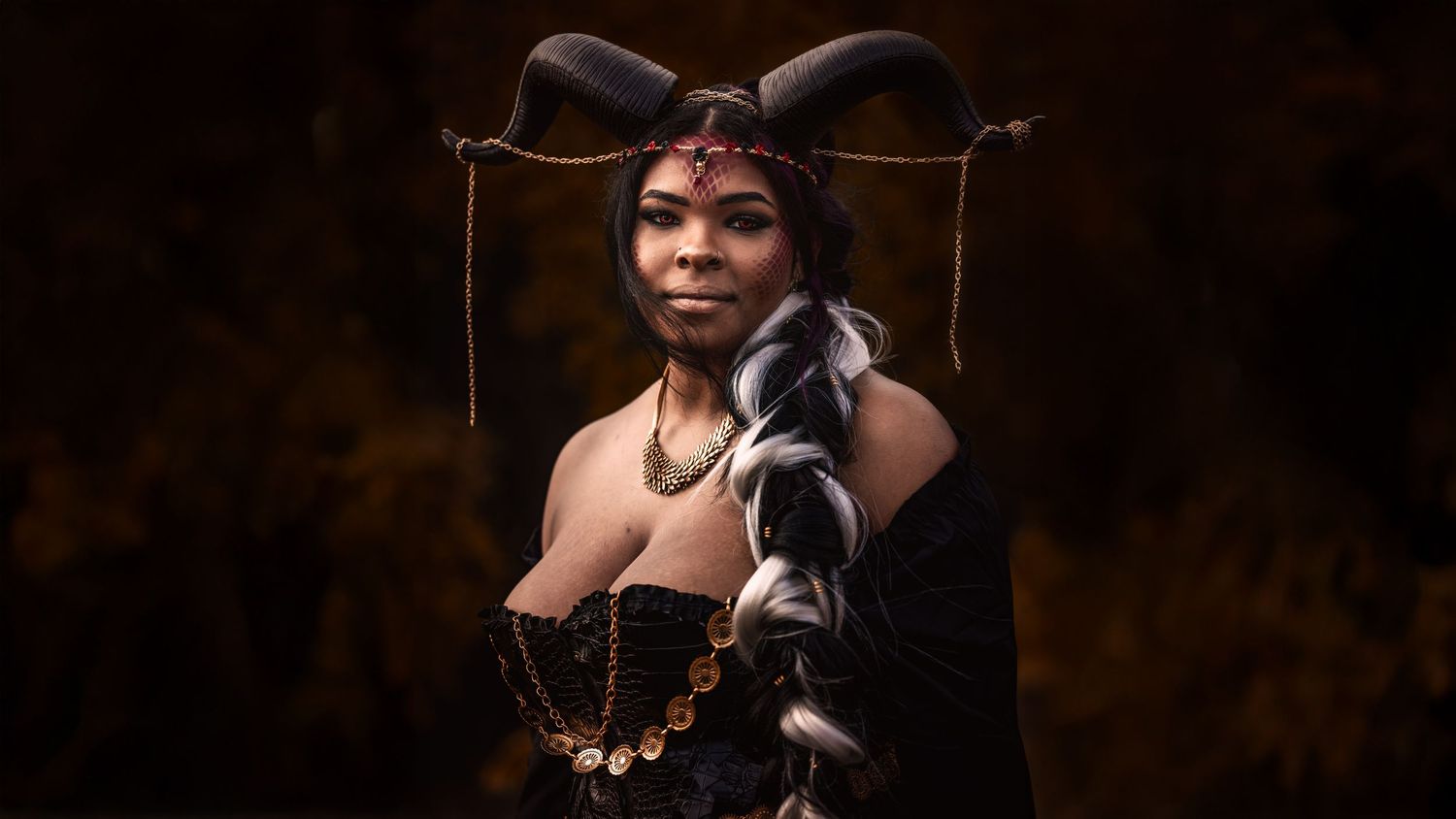 A person wearing elegant jewelry poses in a dark studio setting with dramatic lighting and shadows.