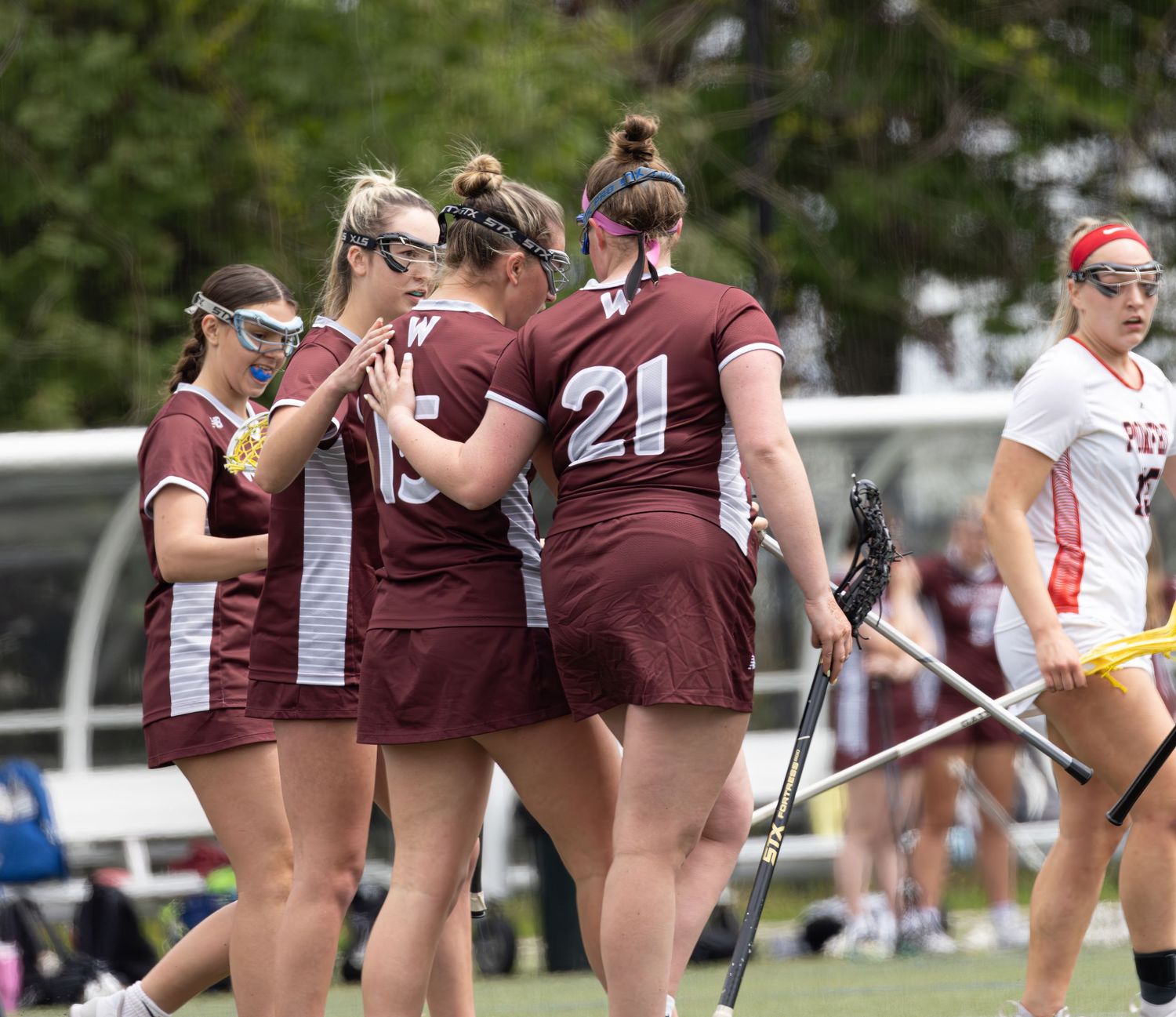 Field hockey players in maroon uniforms compete during an intense match on an outdoor playing field.