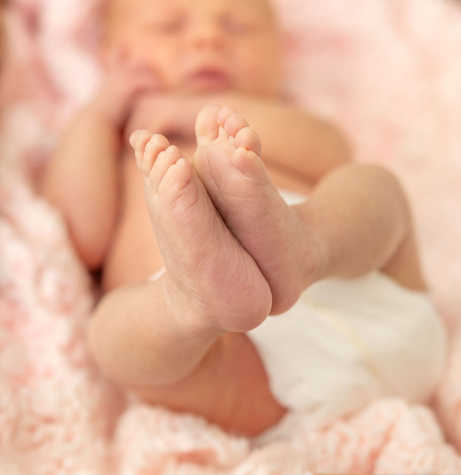 Close-up view of a baby's tiny fingers grasping a soft white blanket in natural light.