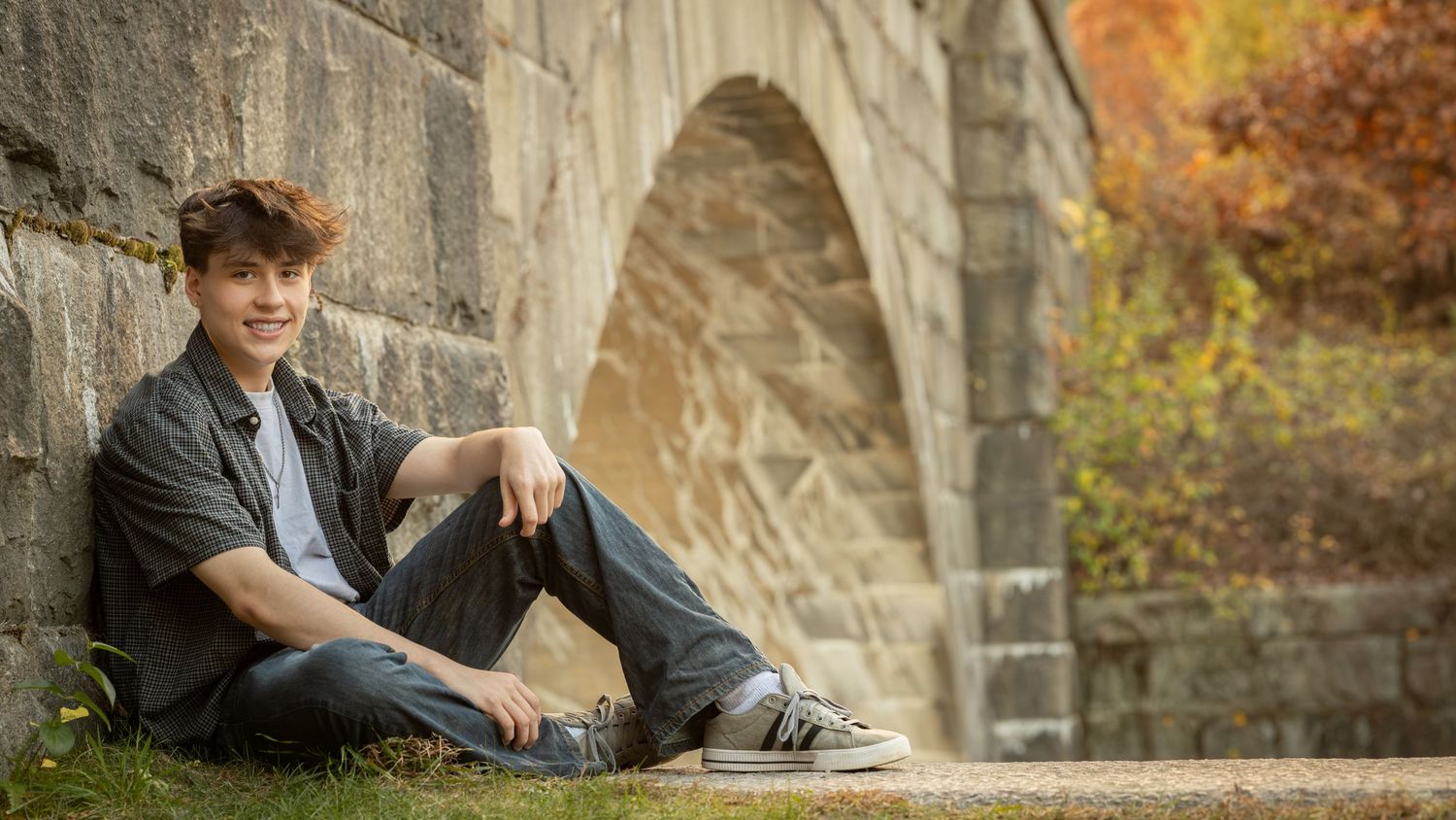 Casual portrait session against stone bridge with autumn foliage in the background.