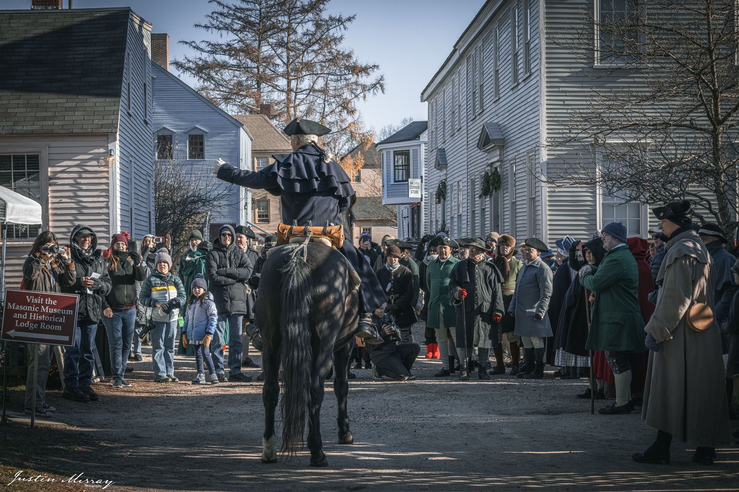 A crowd of people gathered outside historic white buildings in what appears to be a small New England town.