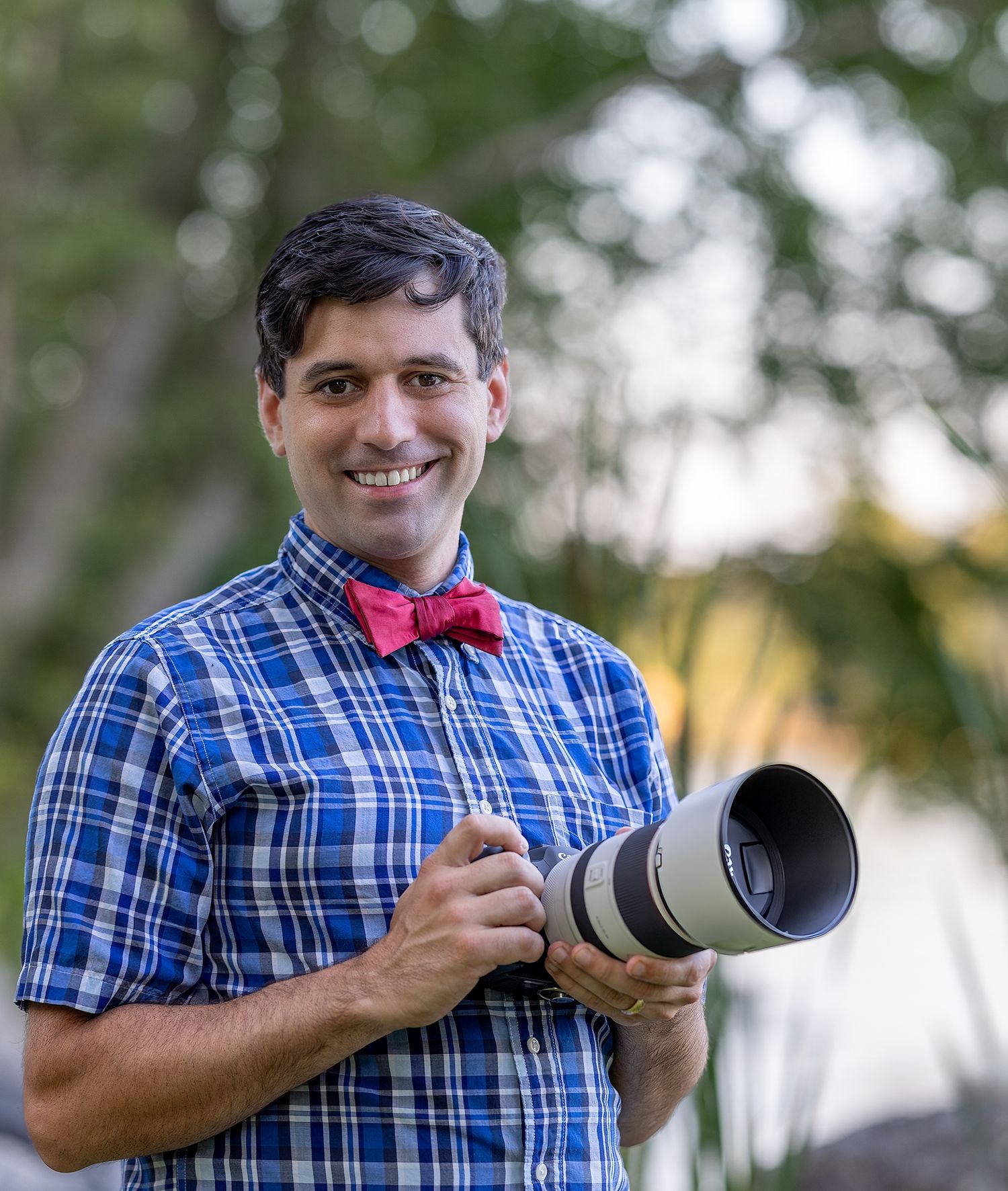 A photographer in a blue plaid shirt holds and demonstrates different positions with a telephoto camera lens.