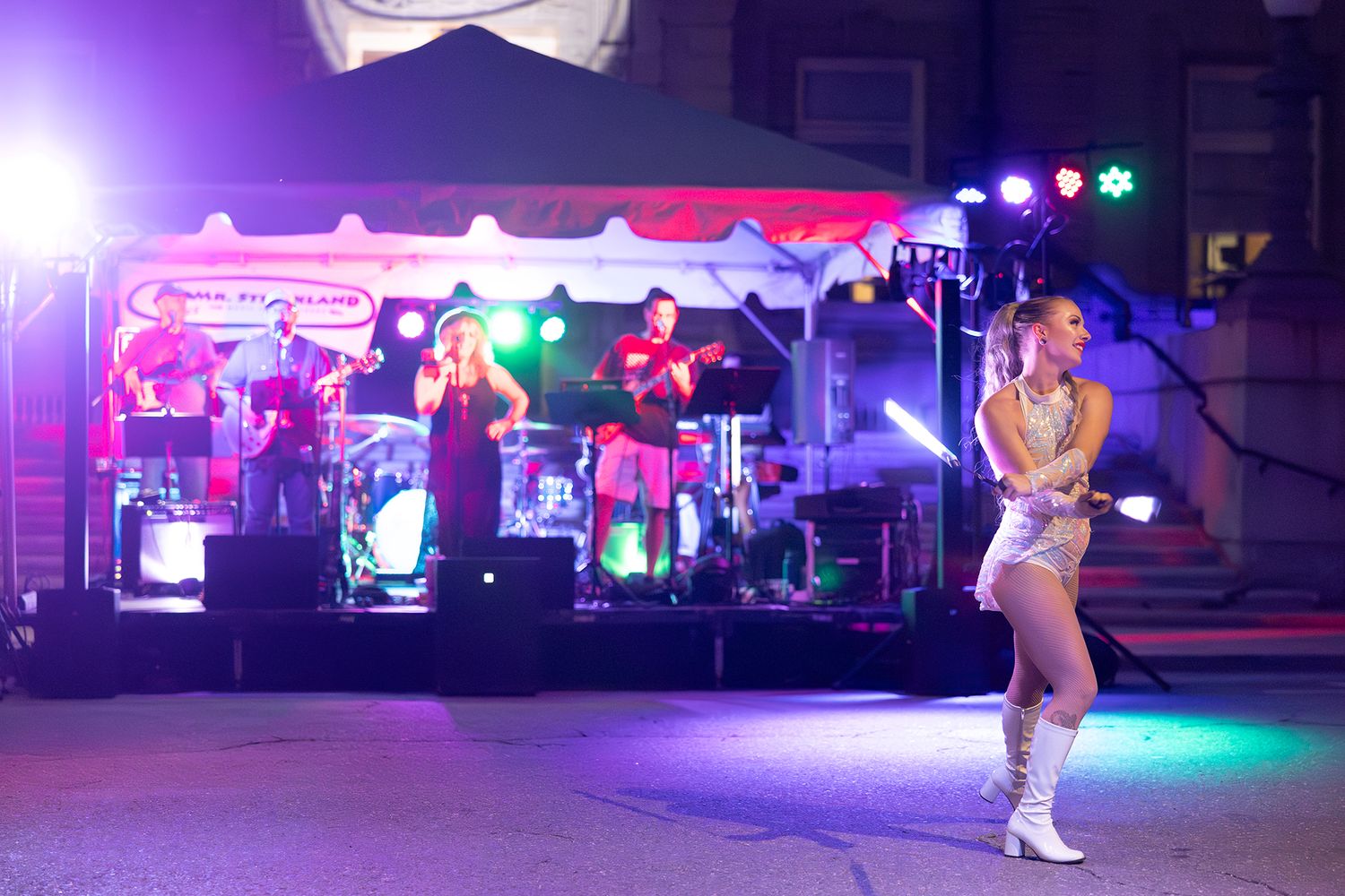 Colorful stage lights illuminate a nighttime concert venue with purple and pink hues creating a vibrant atmosphere.