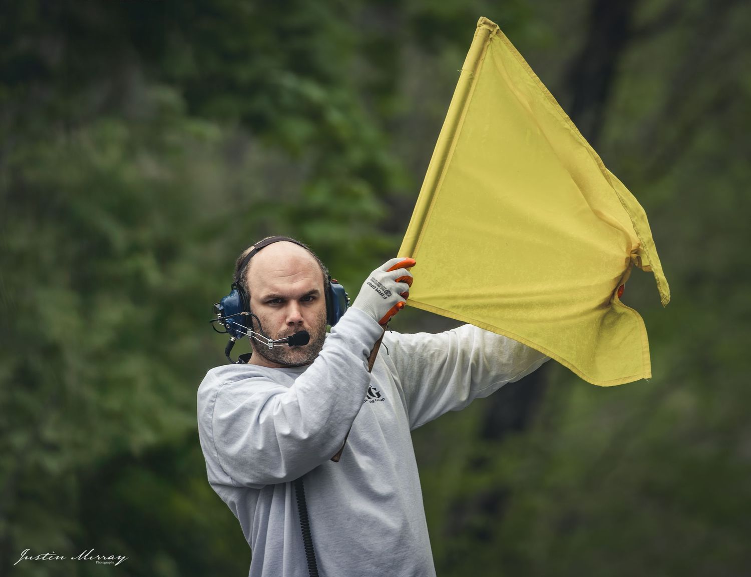 A person in a gray sweatshirt holds up a yellow flag against a green forested background.