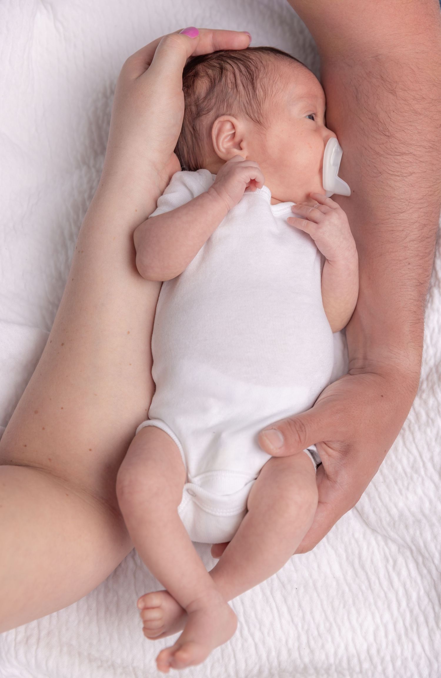 A series of photos showing a newborn baby in white clothing lying on a white blanket while being gently held by adult hands.