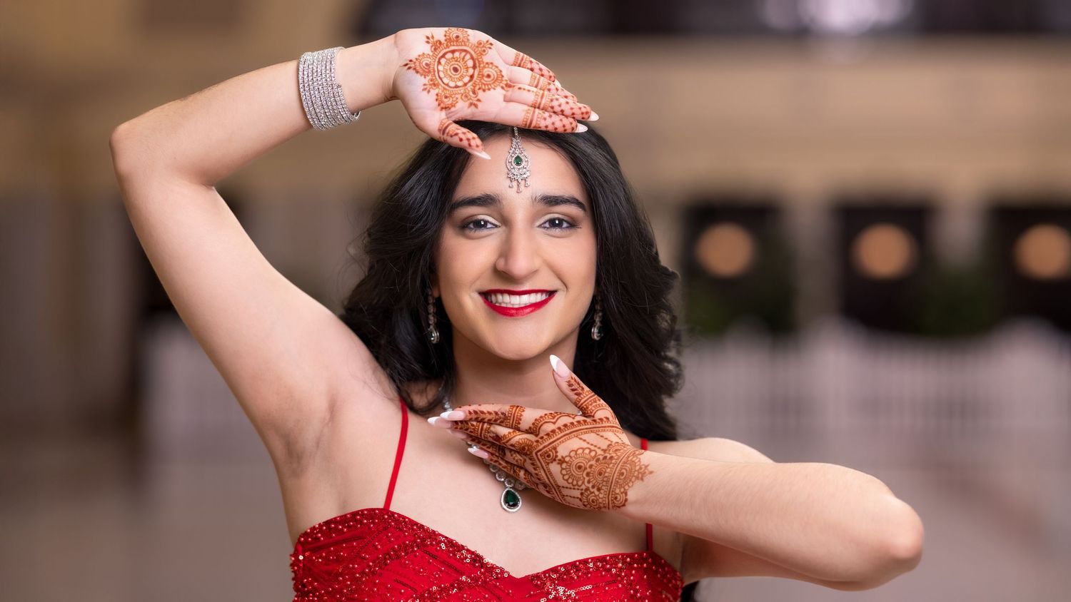 A woman in a red evening gown and black hair poses elegantly against a blurred background.