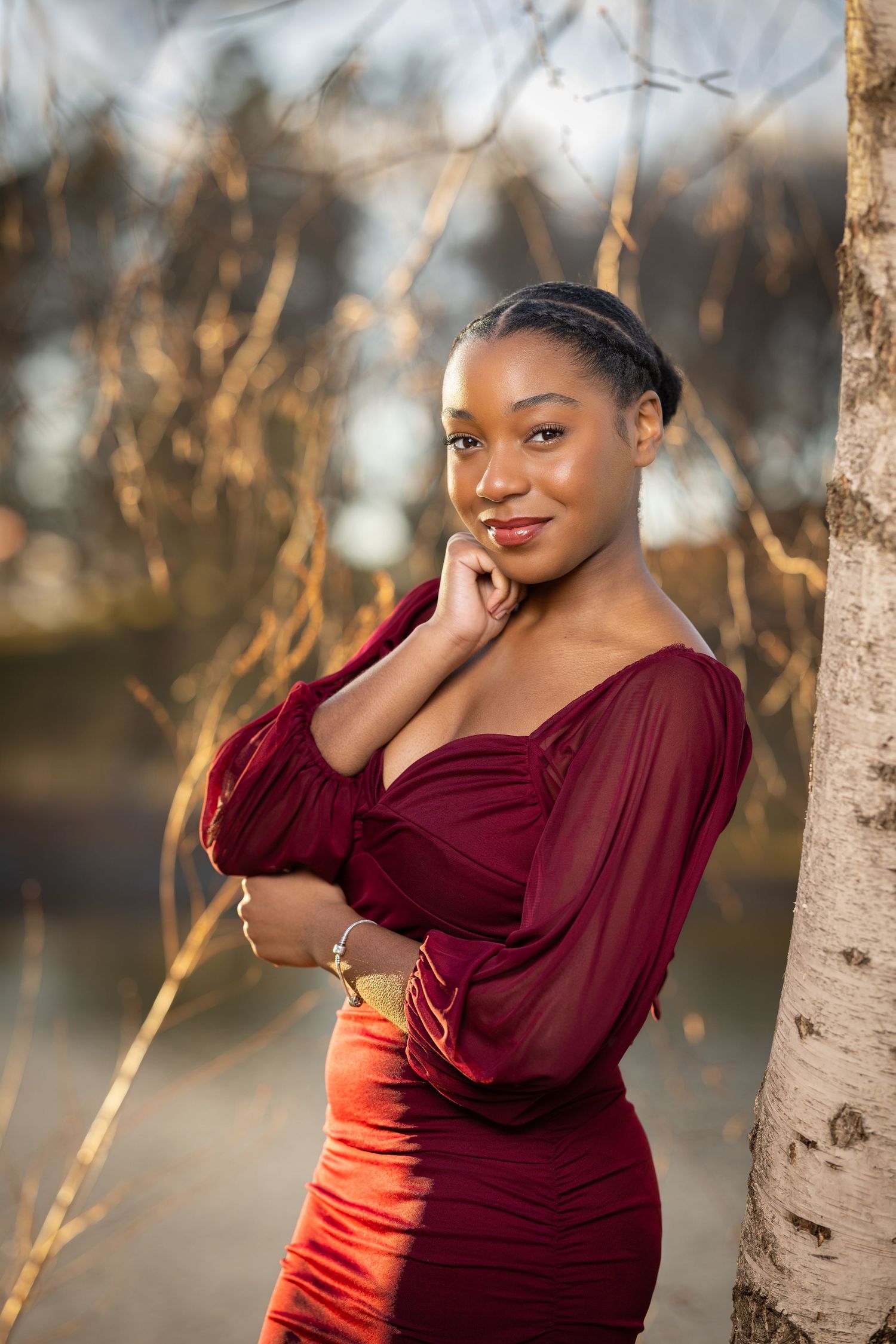 Portrait in burgundy and orange attire posed against birch trees at sunset.