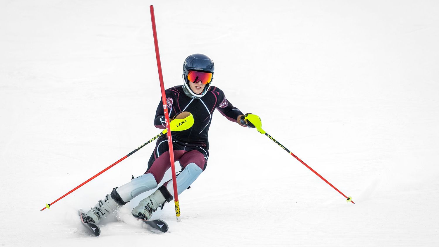 Alpine skier performs a dynamic slalom run on a snowy slope with red gates marking the course.