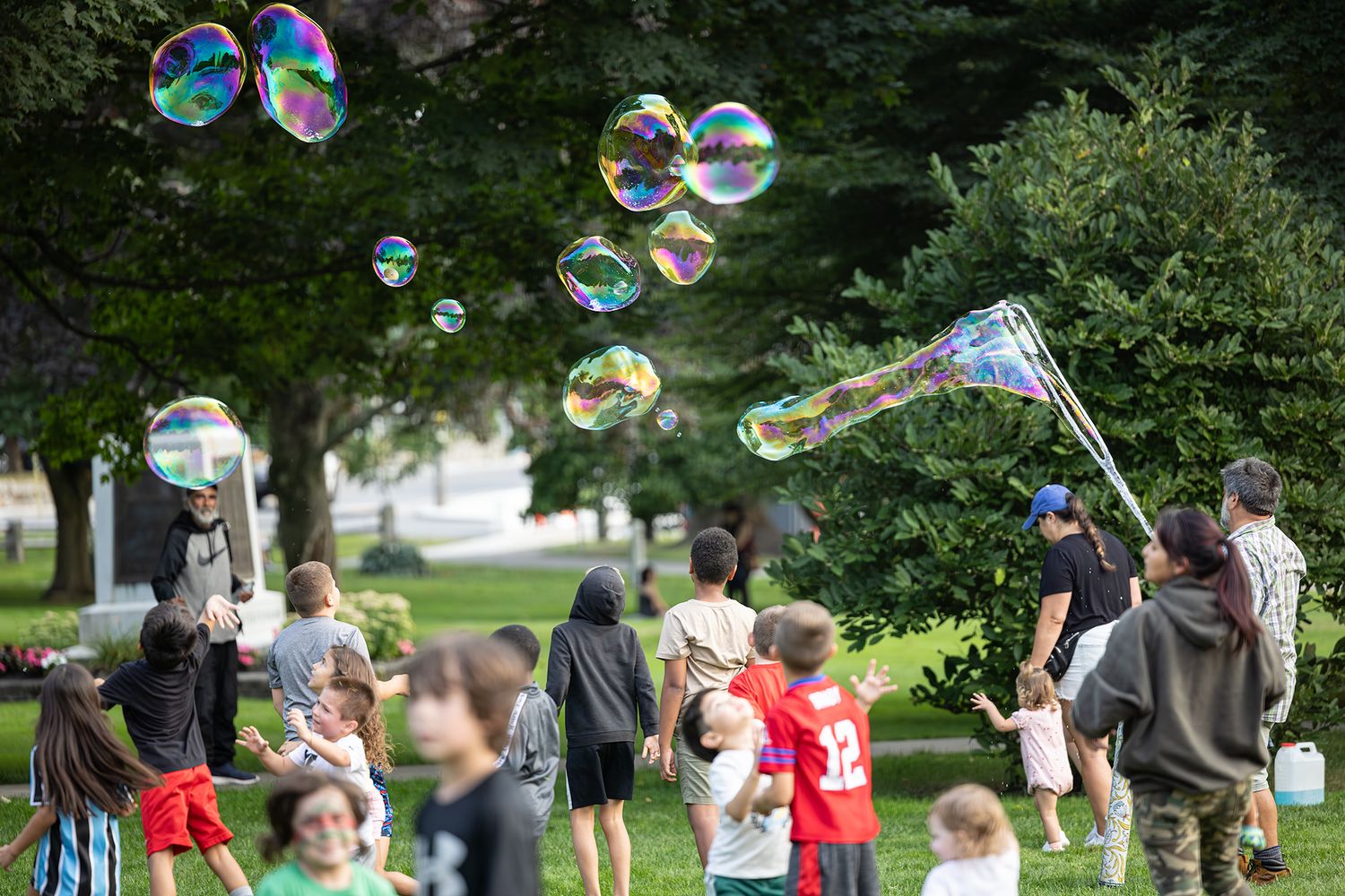 Colorful soap bubbles float through the air in a park setting during a summer day.