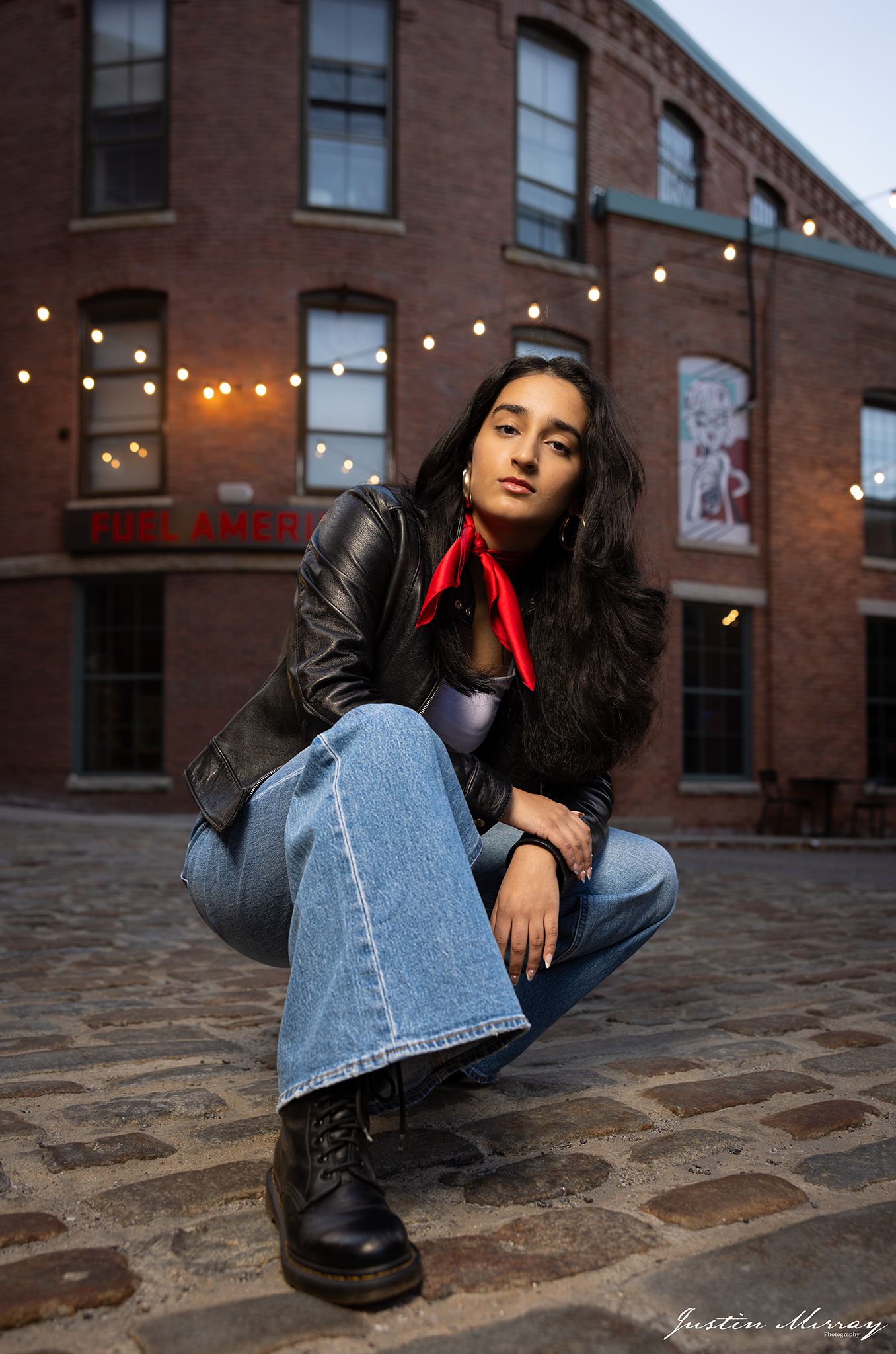 Artistic urban fashion photo series showing poses on cobblestone street with brick building and string lights in background.