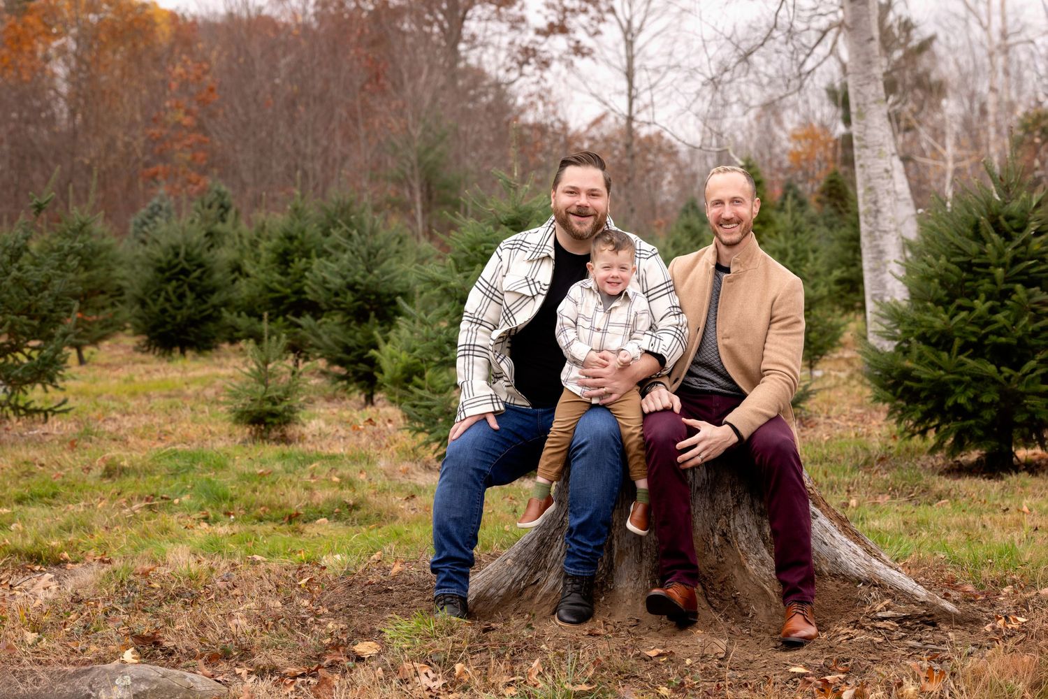 Two people sit together at a Christmas tree farm surrounded by evergreen trees on an autumn day.