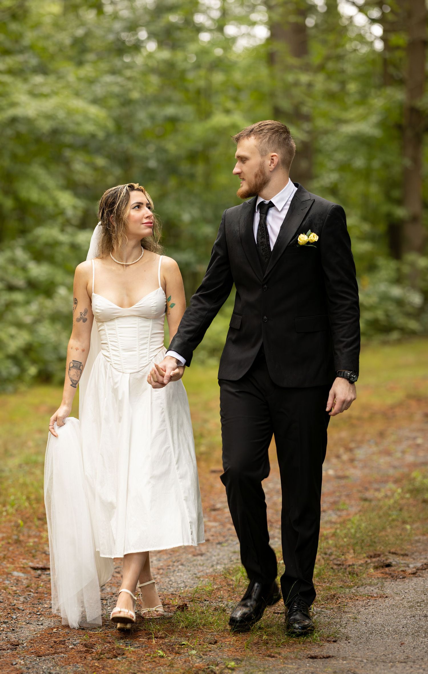 A bride and groom walk together on a wooded path during their outdoor wedding photo session.