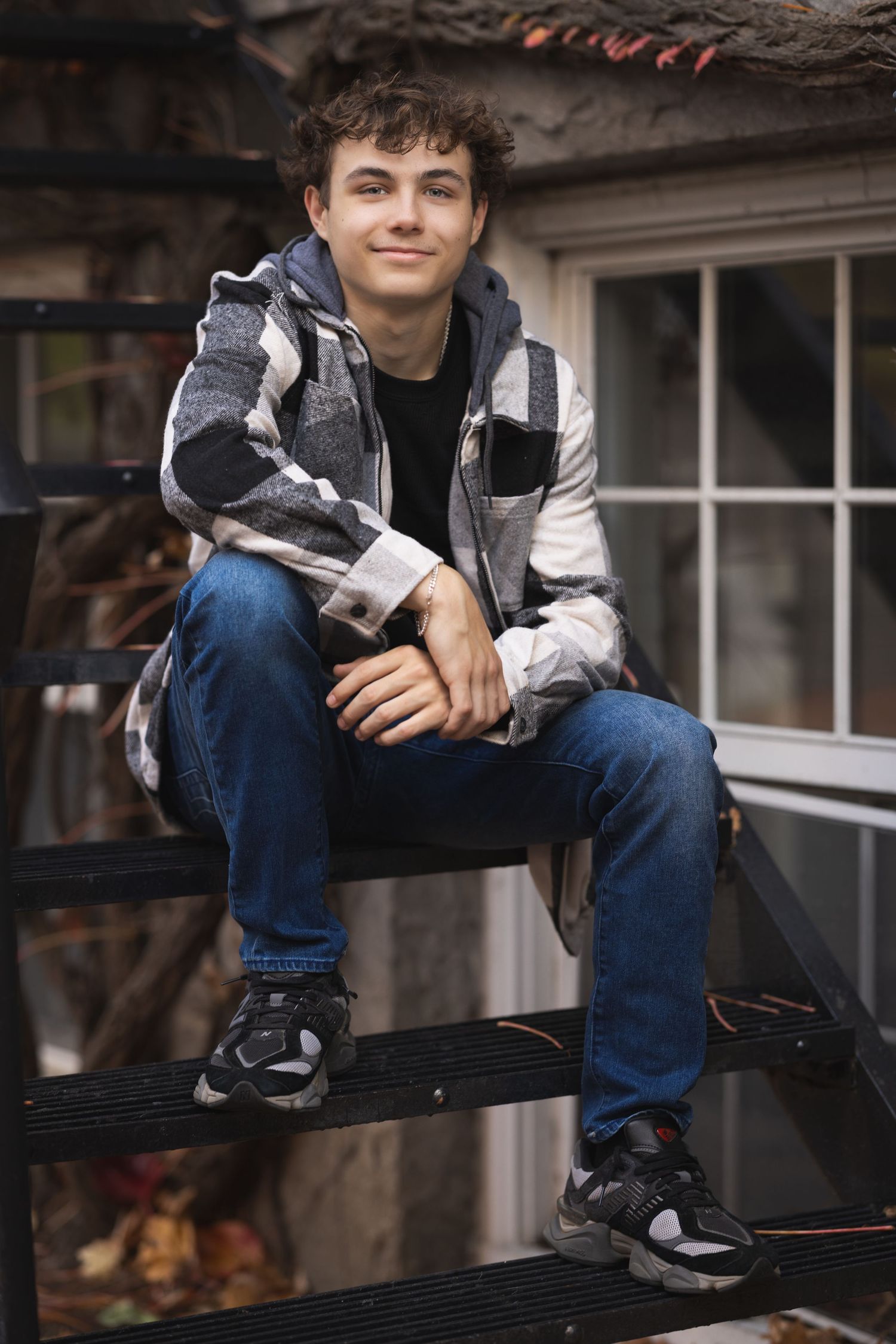 Person sitting casually on black bench wearing jeans and plaid shirt against rustic building.
