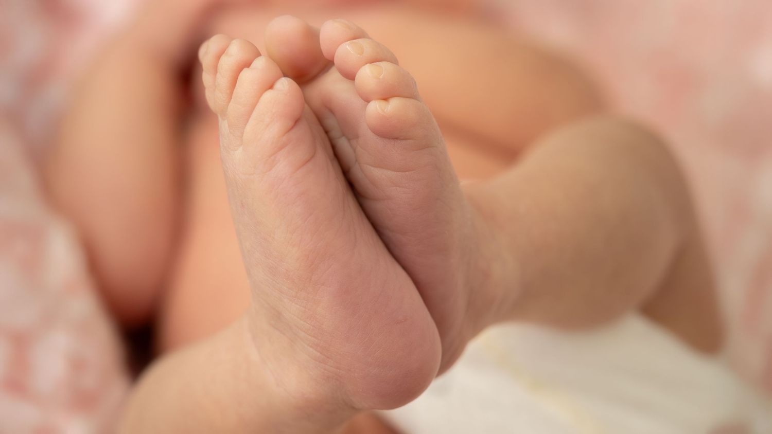 Close-up macro photo of a baby's tiny hand grasping an adult finger against a soft blurred background.