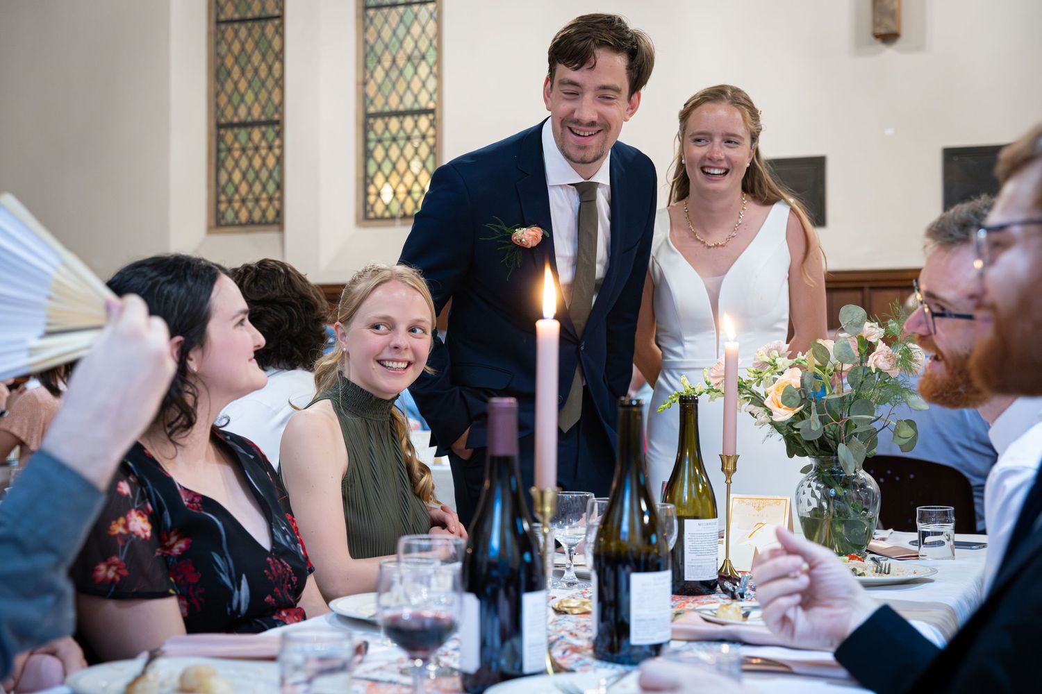 Guests enjoying a formal dinner reception at a banquet table with wine bottles and floral centerpieces.
