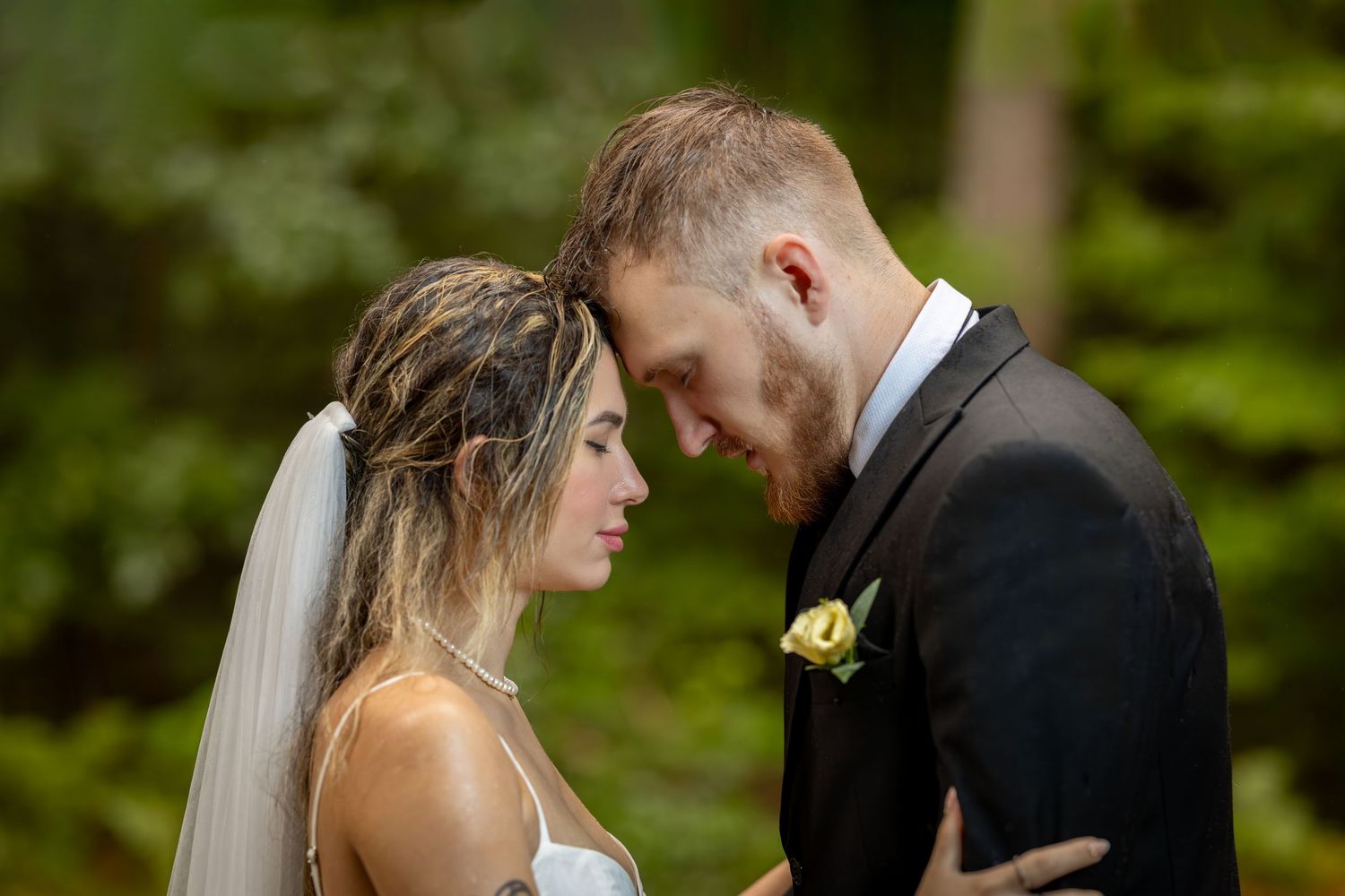 A couple shares an intimate moment in a lush forest setting during their wedding ceremony.